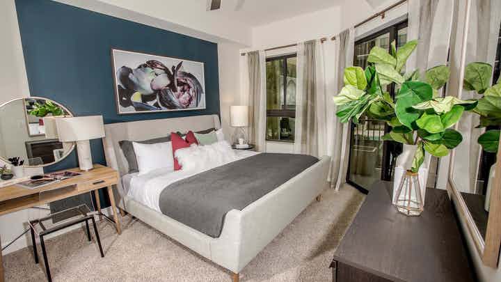 Interior view of an AMLI Joya apartment bedroom with a bed underneath wall art, side desk and windows