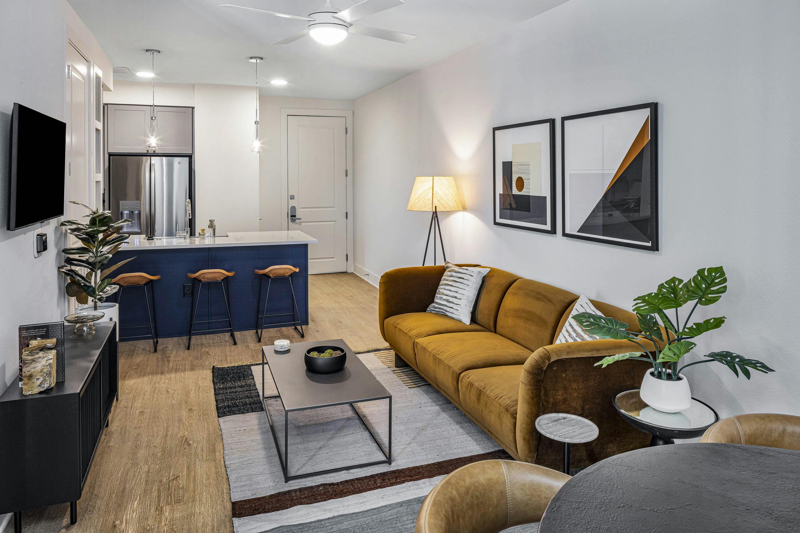 AMLI Branch Park living room with rust color couch across form TV and white countertop island with navy base and stools