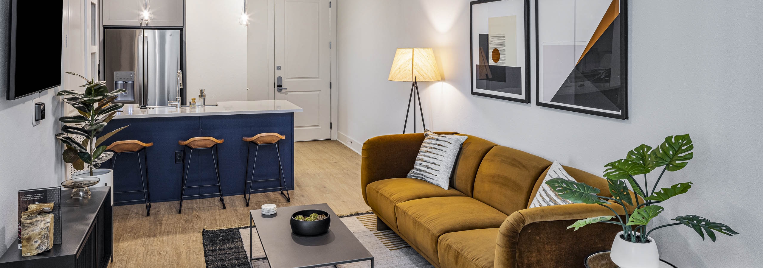 AMLI Branch Park living room with rust color couch across form TV and white countertop island with navy base and stools