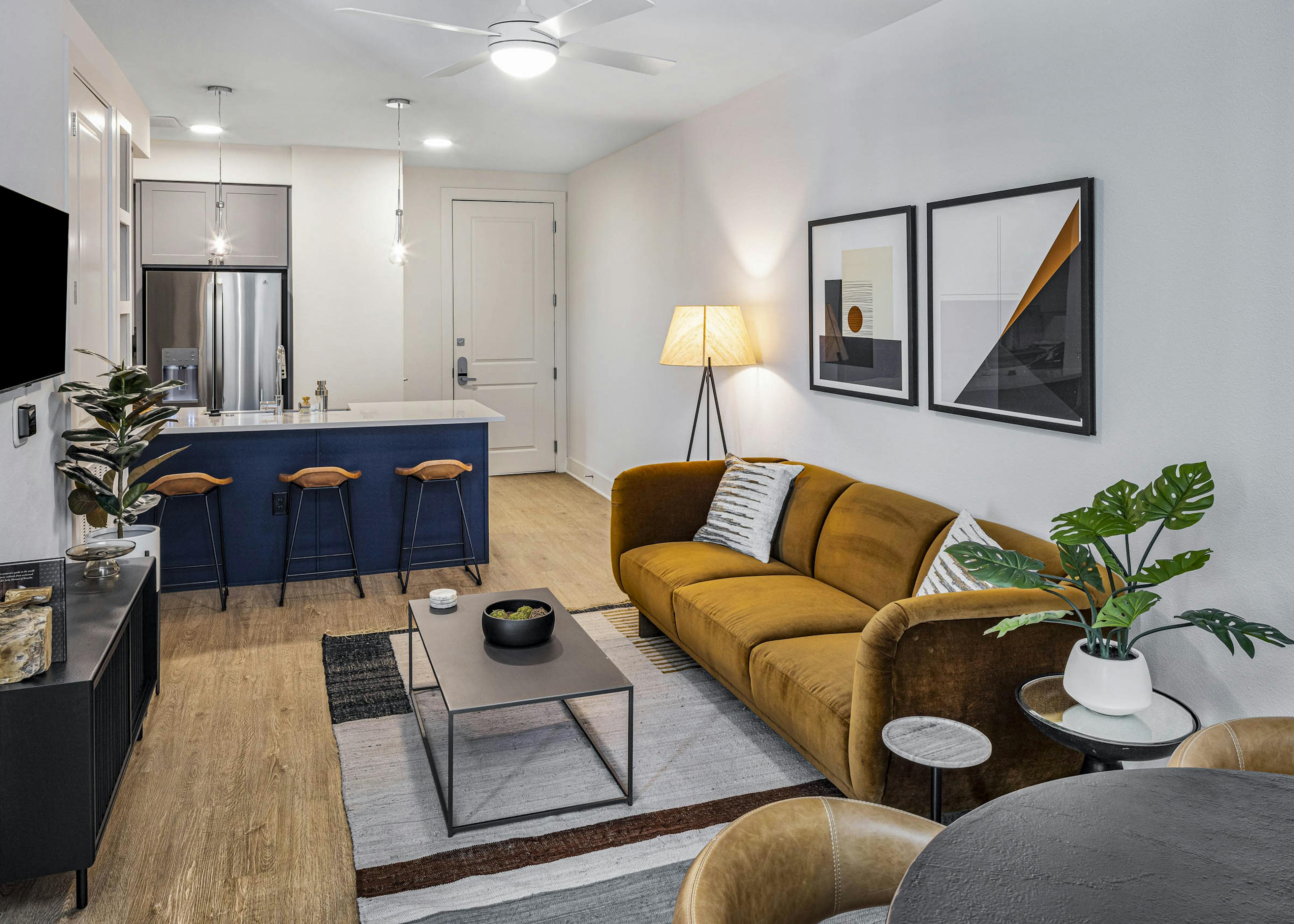 AMLI Branch Park living room with rust color couch across form TV and white countertop island with navy base and stools
