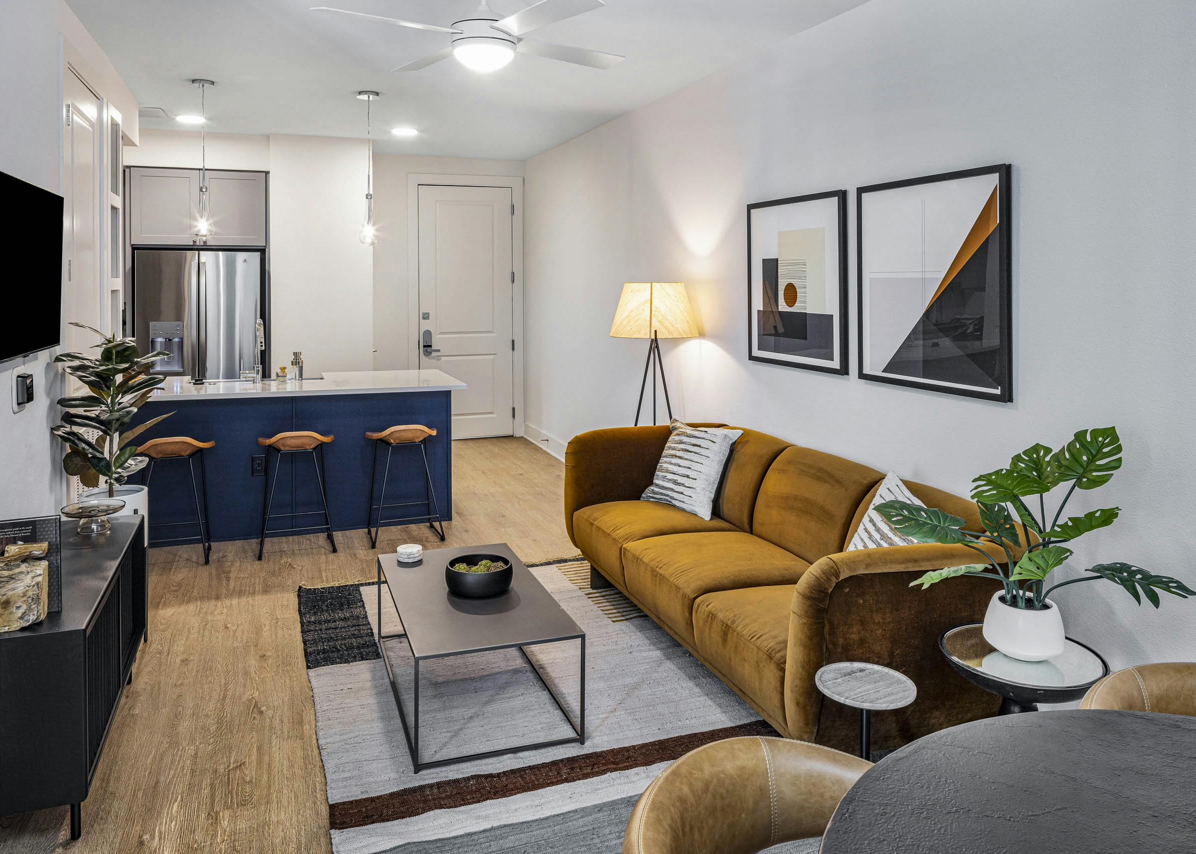 AMLI Branch Park living room with rust color couch across form TV and white countertop island with navy base and stools