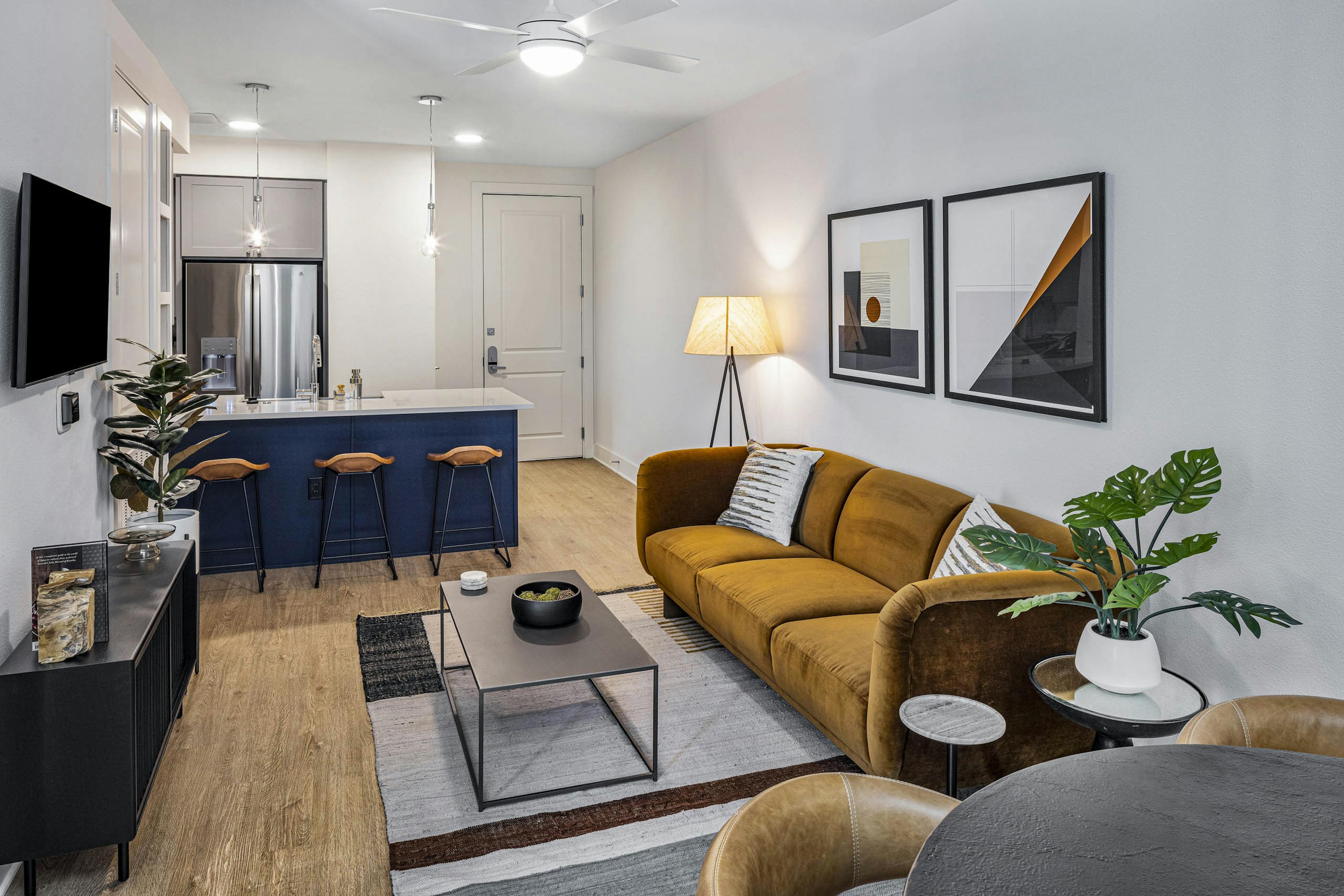 AMLI Branch Park living room with rust color couch across form TV and white countertop island with navy base and stools