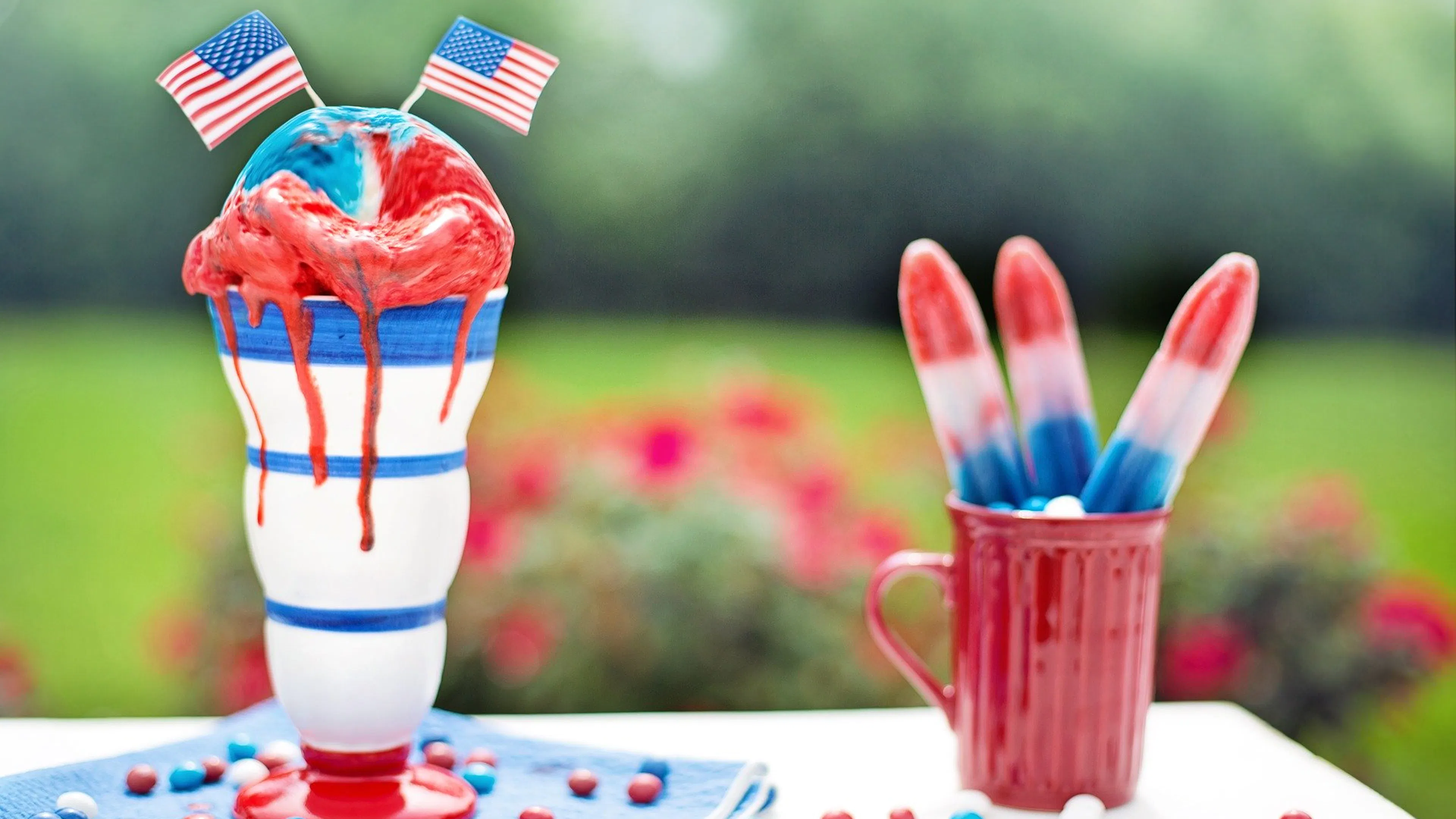 Two tall sundae glasses filled with red and blue ice cream and little American flags sticking out the top