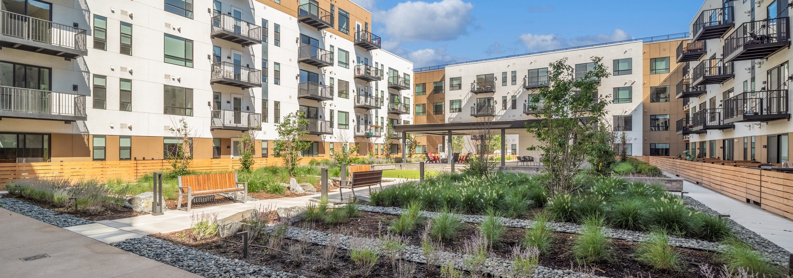 View of lush courtyard garden with rows of green vegetation and grey river rock with bench seating at AMLI Broadway Park
