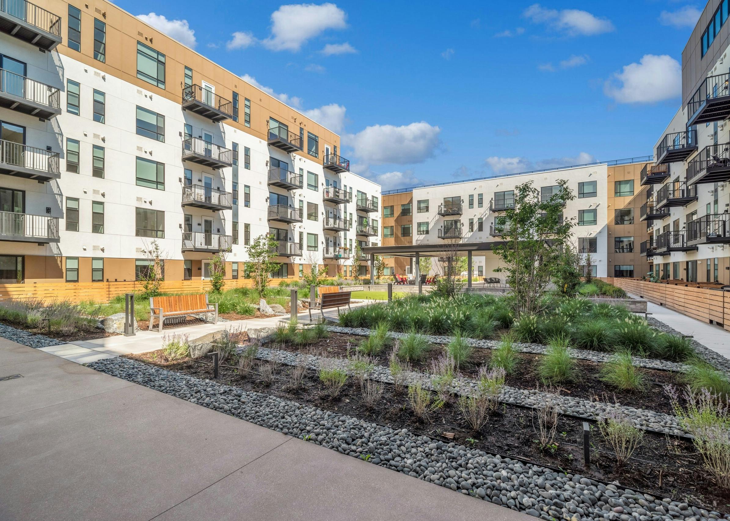 View of lush courtyard garden with rows of green vegetation and grey river rock with bench seating at AMLI Broadway Park