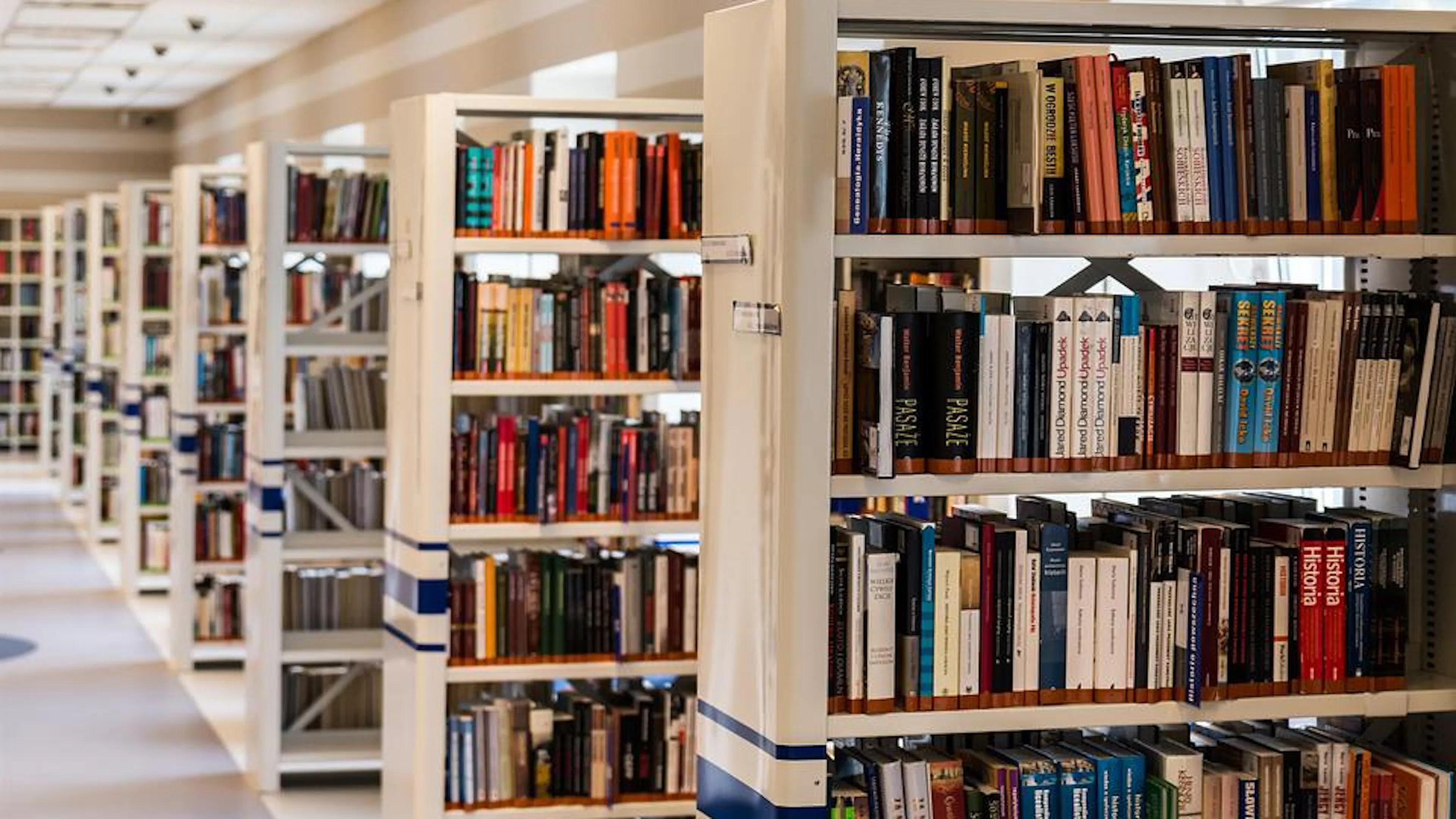 Long rows of library shelves with books stacked in them in a well lit hall