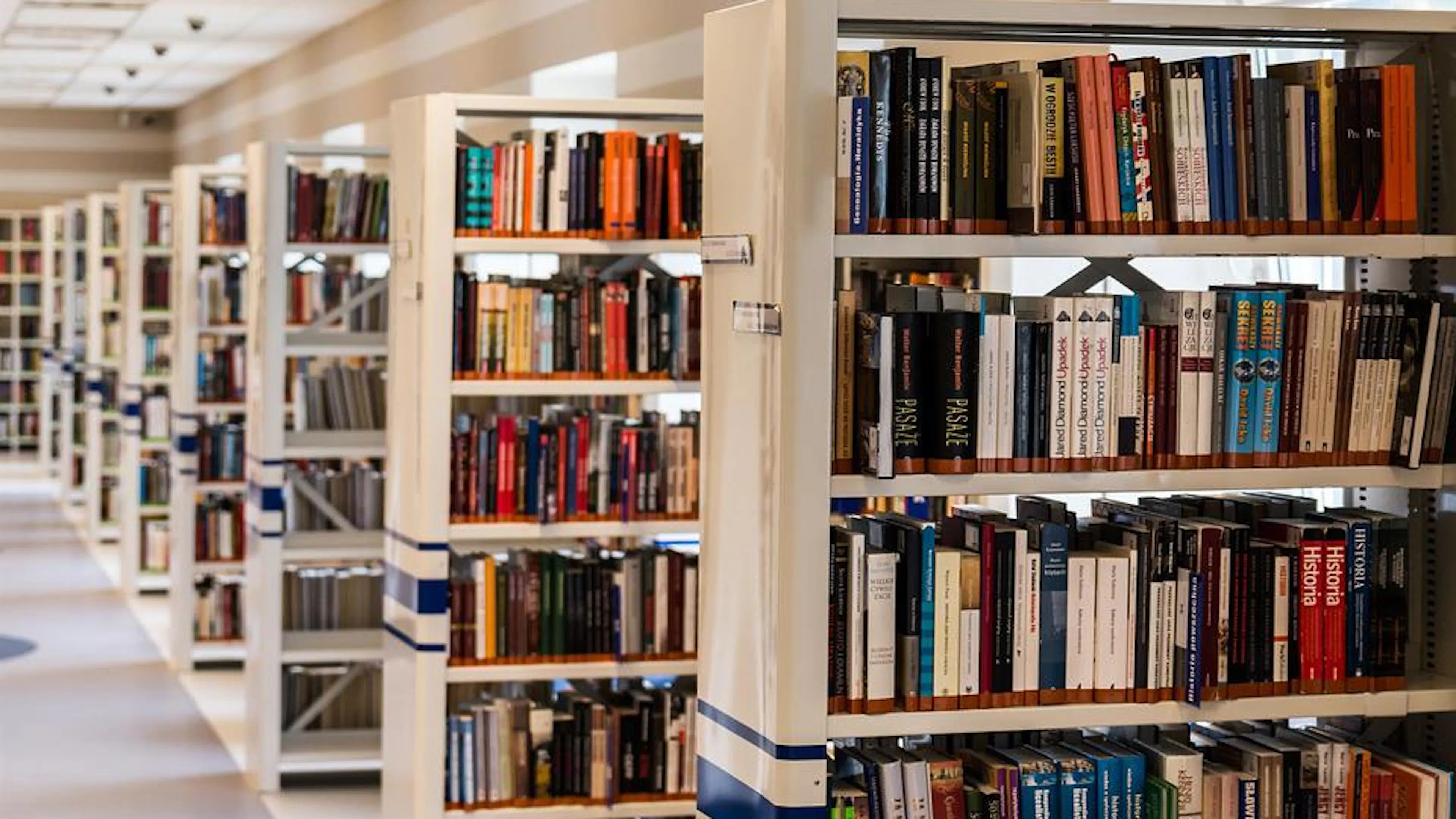 Long rows of library shelves with books stacked in them in a well lit hall