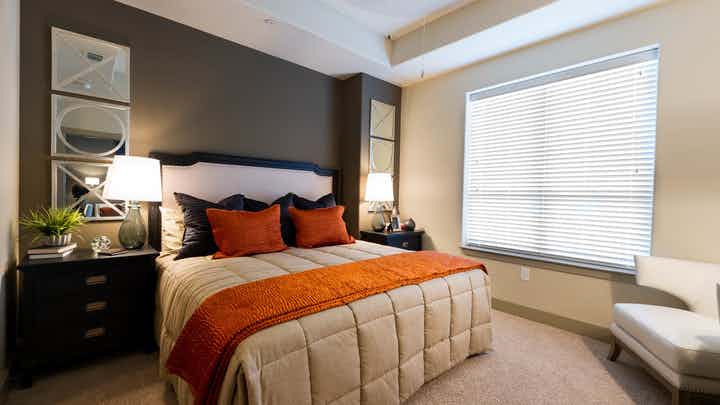 Interior view of bedroom at AMLI River Oaks apartment building with bed, two nightstands with lamps and window with blinds
