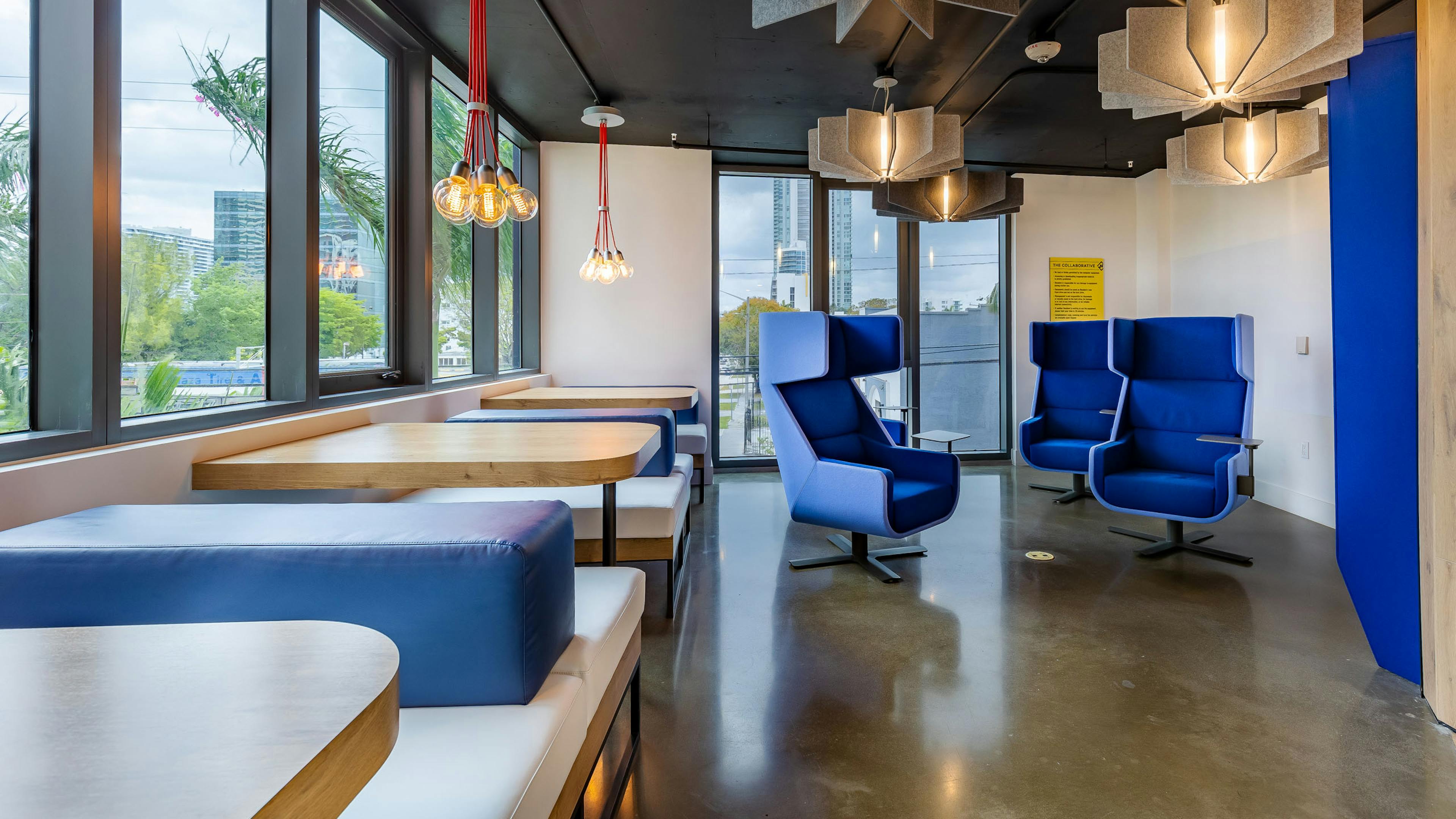Workspace at AMLI Midtown Miami apartments with booth seating along windows and hanging lights and angular blue armchairs 
