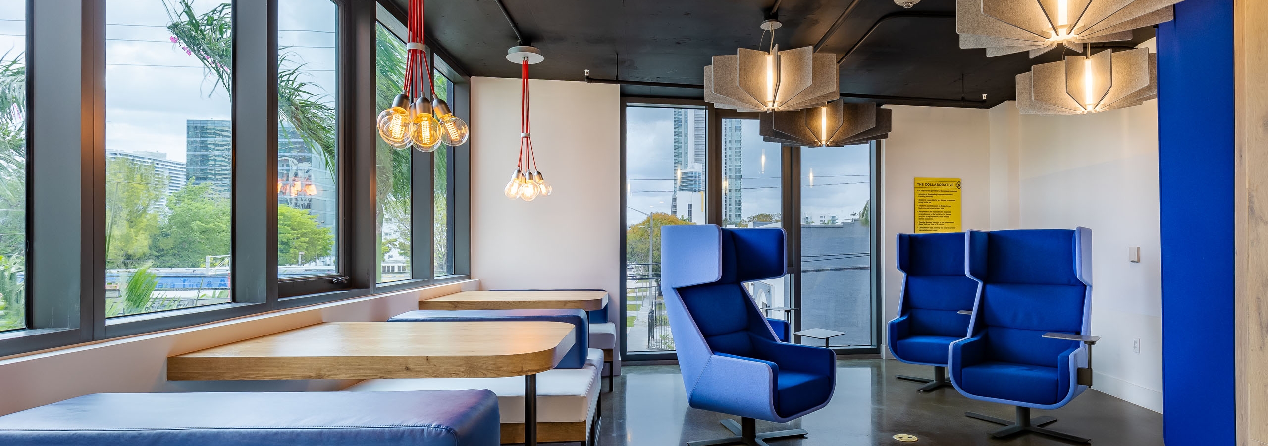Workspace at AMLI Midtown Miami apartments with booth seating along windows and hanging lights and angular blue armchairs