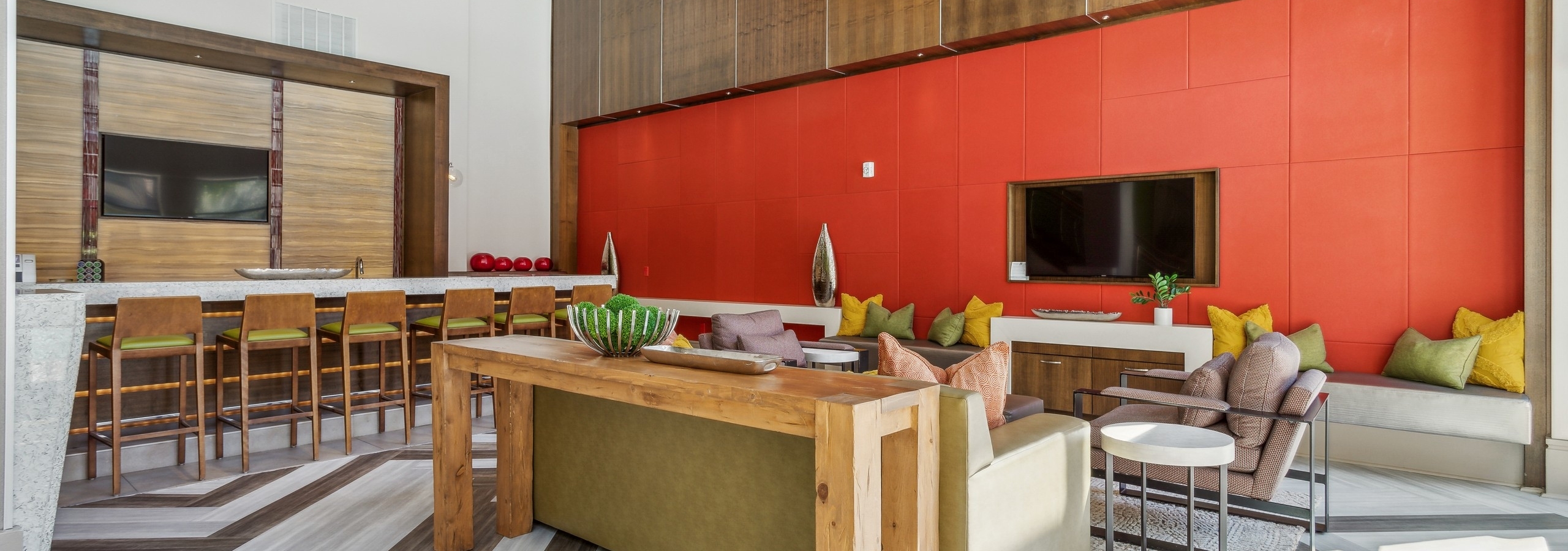 AMLI Ponce Park clubroom with seating in front of orange wall with TV and serving kitchen with stools facing a TV