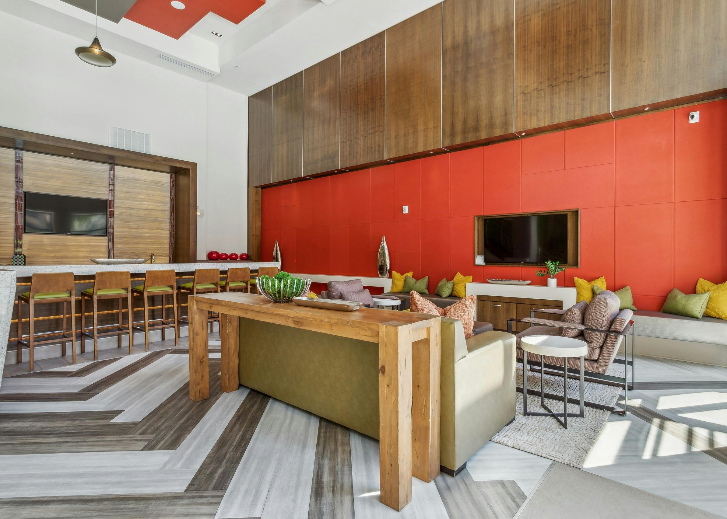AMLI Ponce Park clubroom with seating in front of orange wall with TV and serving kitchen with stools facing a TV