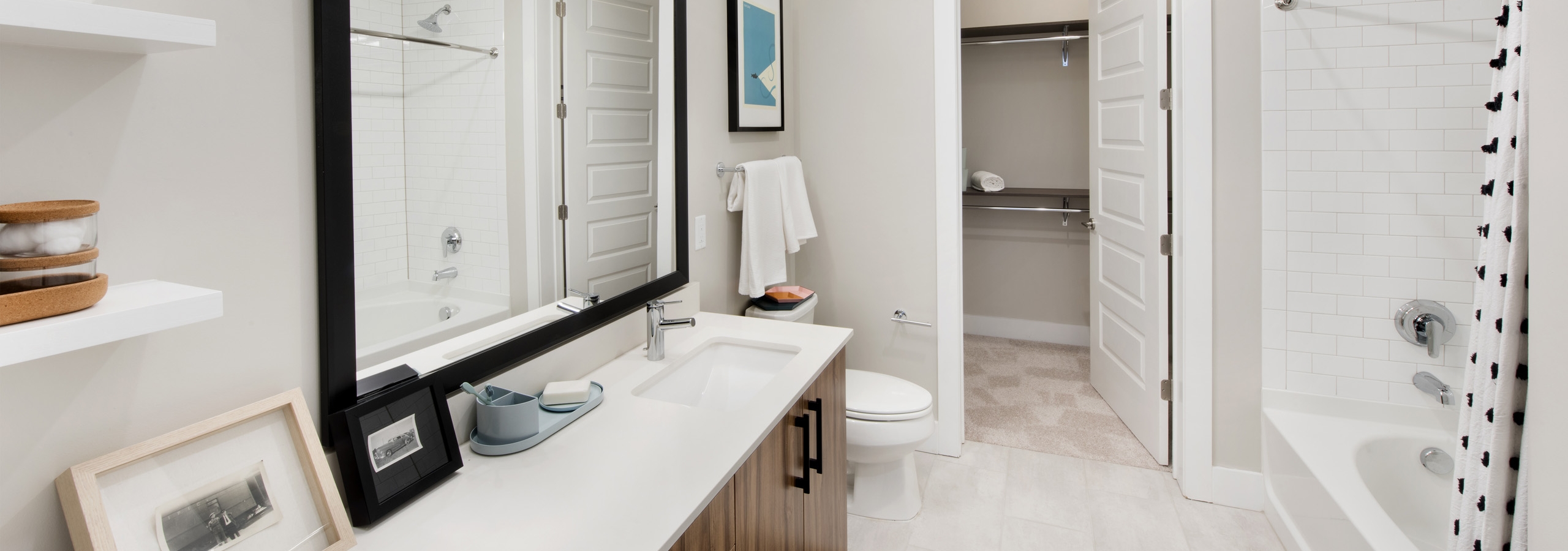 AMLI Lenox apartment bathroom with mirror over dark wood vanity with light countertop and large garden tub and walk in closet