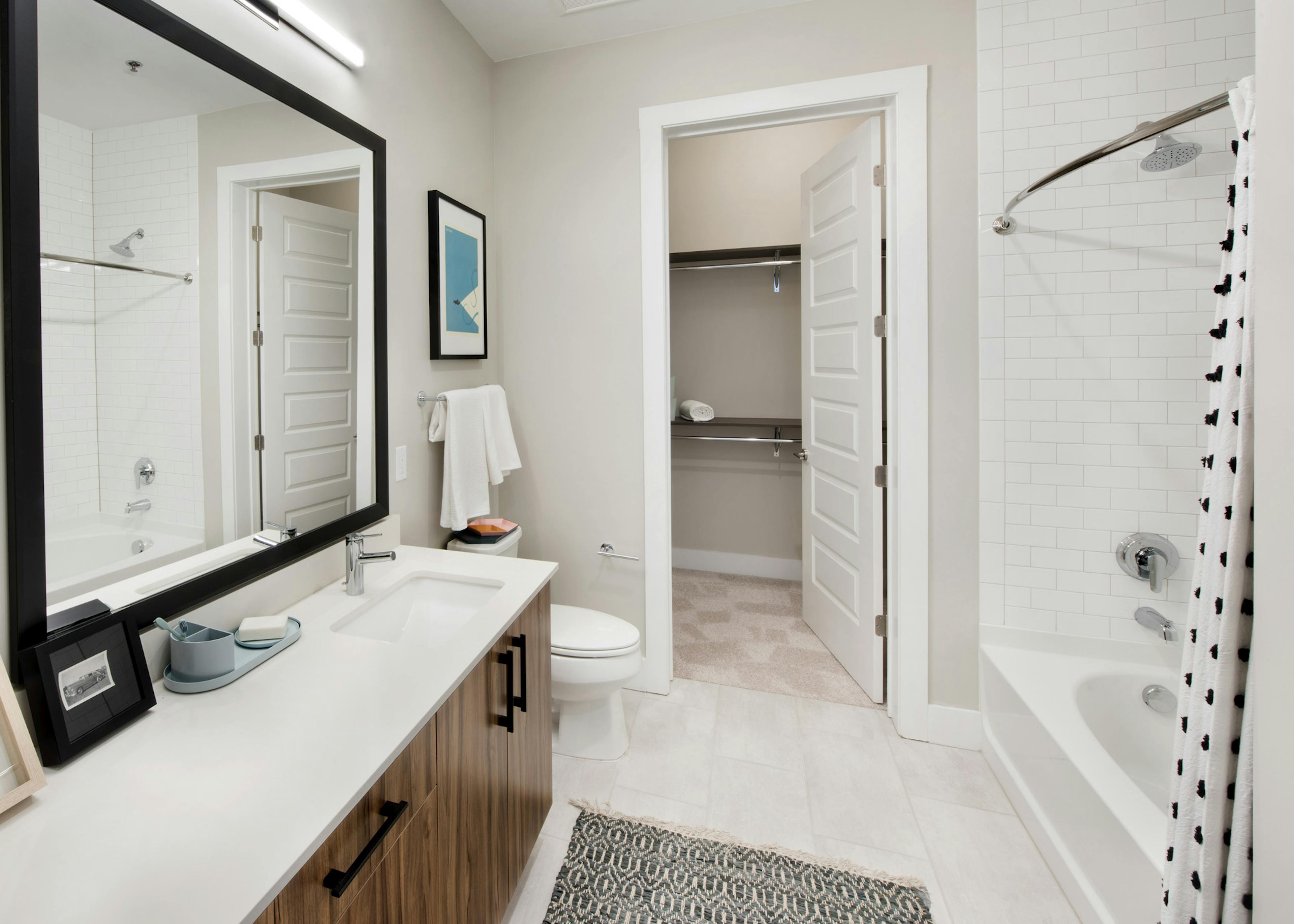 AMLI Lenox apartment bathroom with mirror over dark wood vanity with light countertop and large garden tub and walk in closet