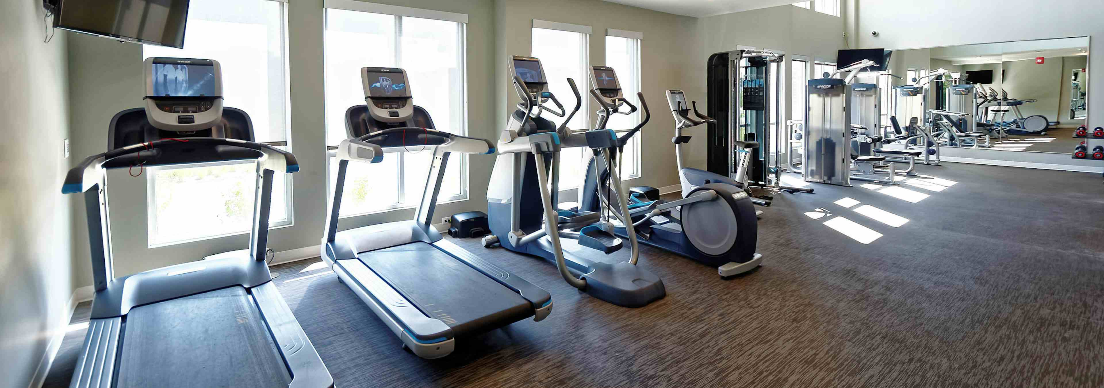 Interior view of fitness center at AMLI Dry Creek apartments with multiple treadmills and elliptical machines and windows