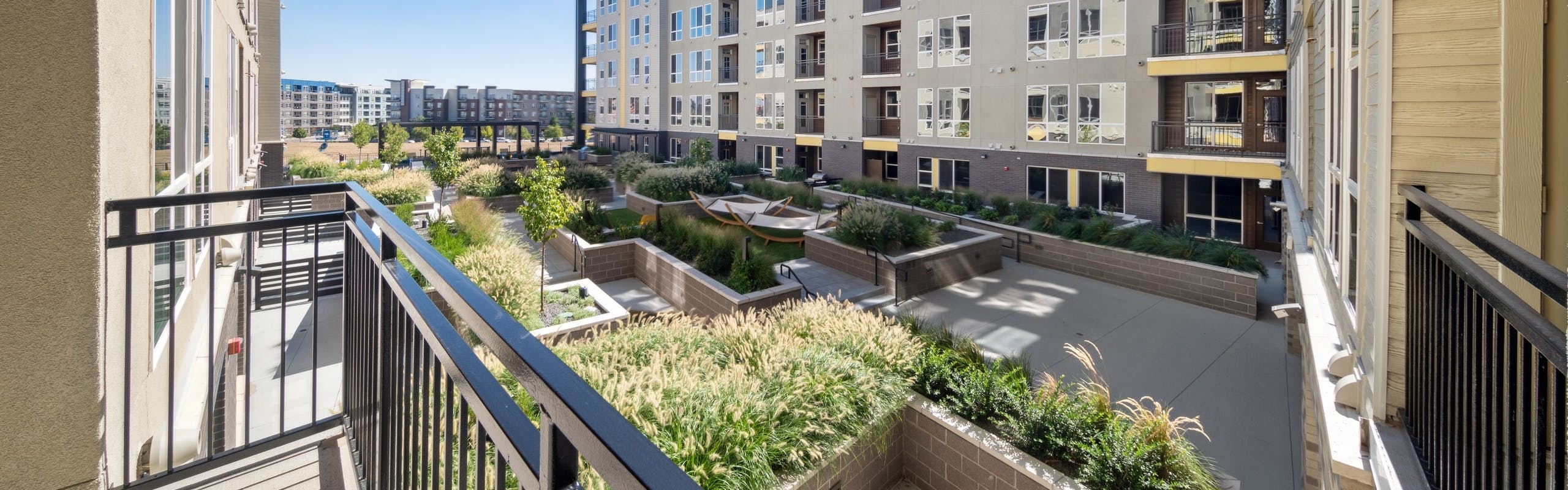 Balcony at AMLI RiNo apartments overlooking lushly landscaped courtyard with planters and hammocks and blue sky above