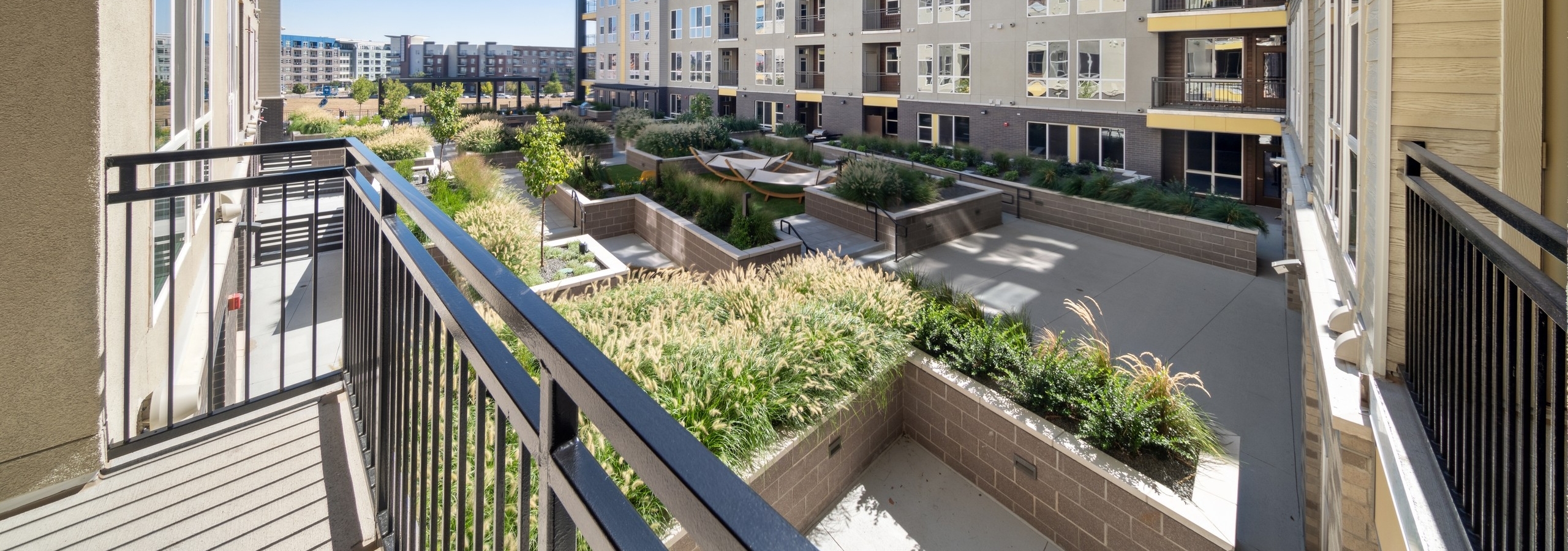 Balcony at AMLI RiNo apartments overlooking lushly landscaped courtyard with planters and hammocks and blue sky above