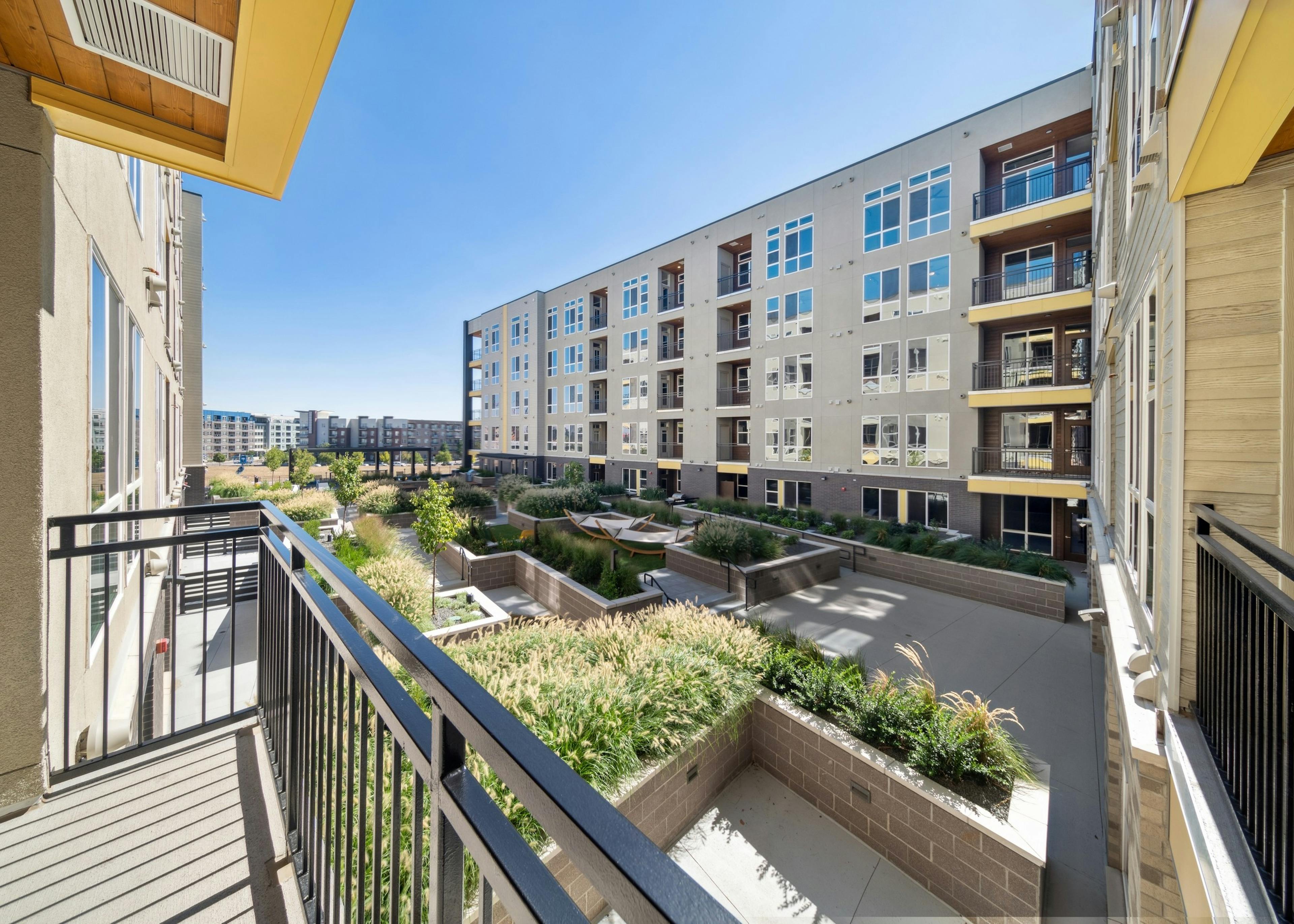 Balcony at AMLI RiNo apartments overlooking lushly landscaped courtyard with planters and hammocks and blue sky above