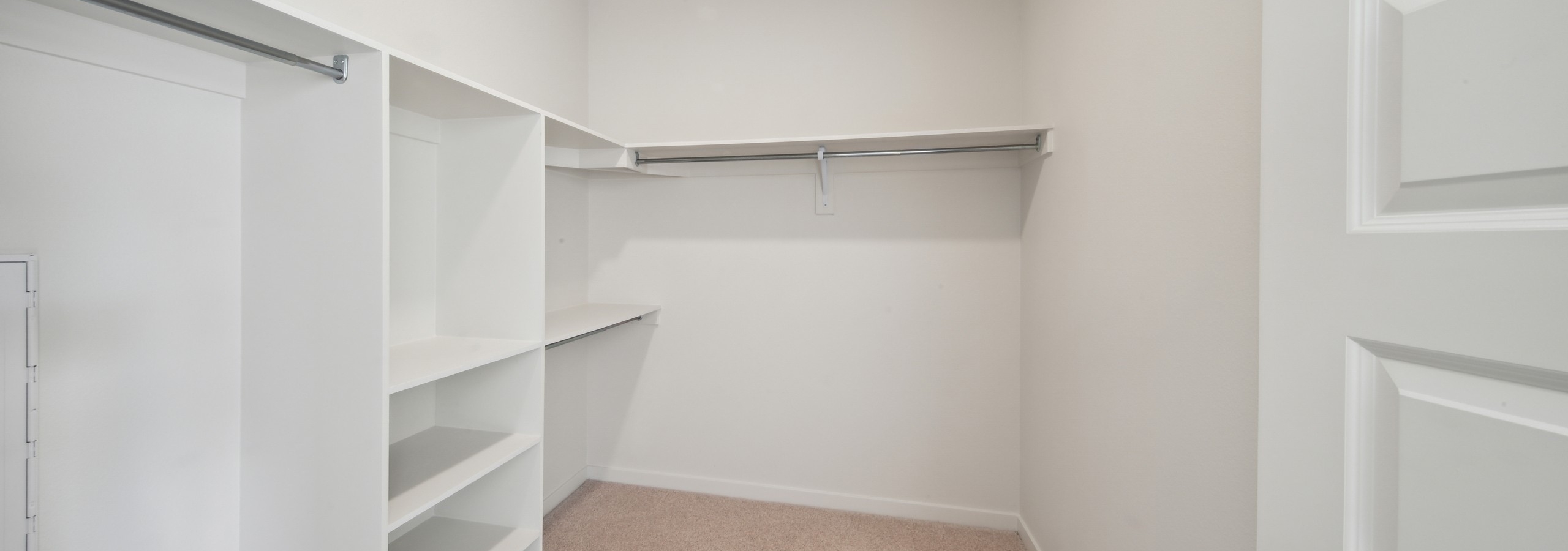 Interior view of AMLI Broadway Park walk in closet with built in shelves and hanging poles and beige carpeted floor
