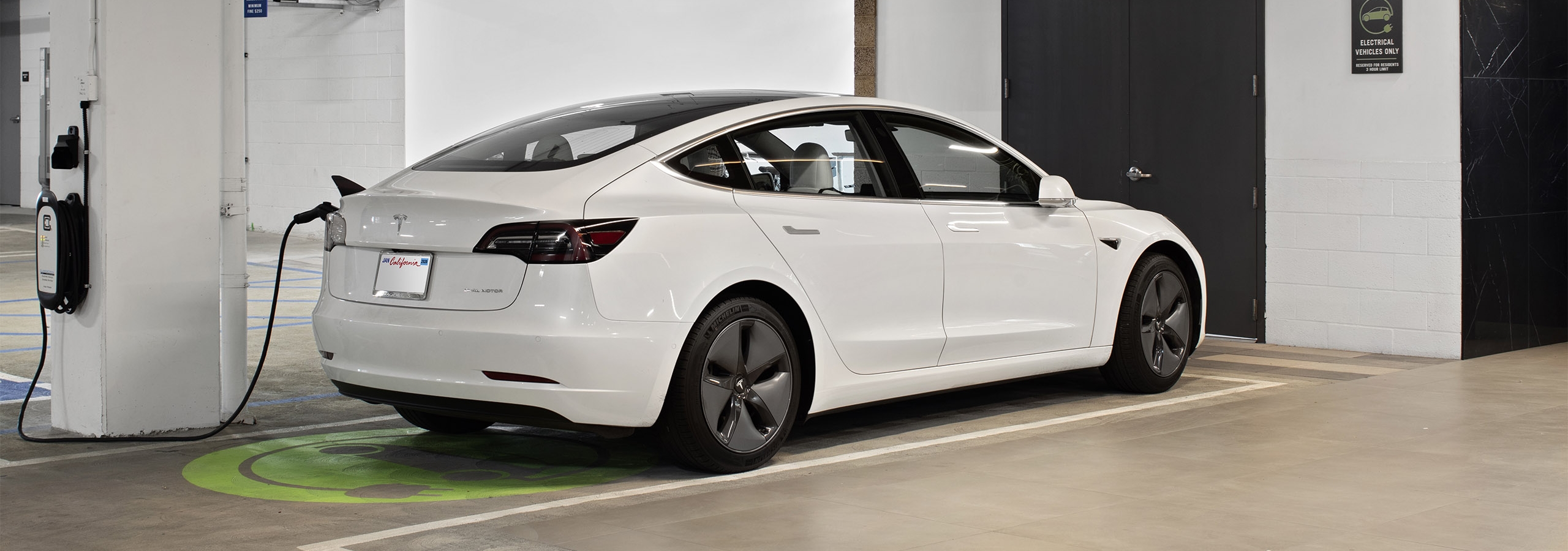 Electric vehicle charging station at AMLI Park Broadway apartments with white Tesla connected to charging station