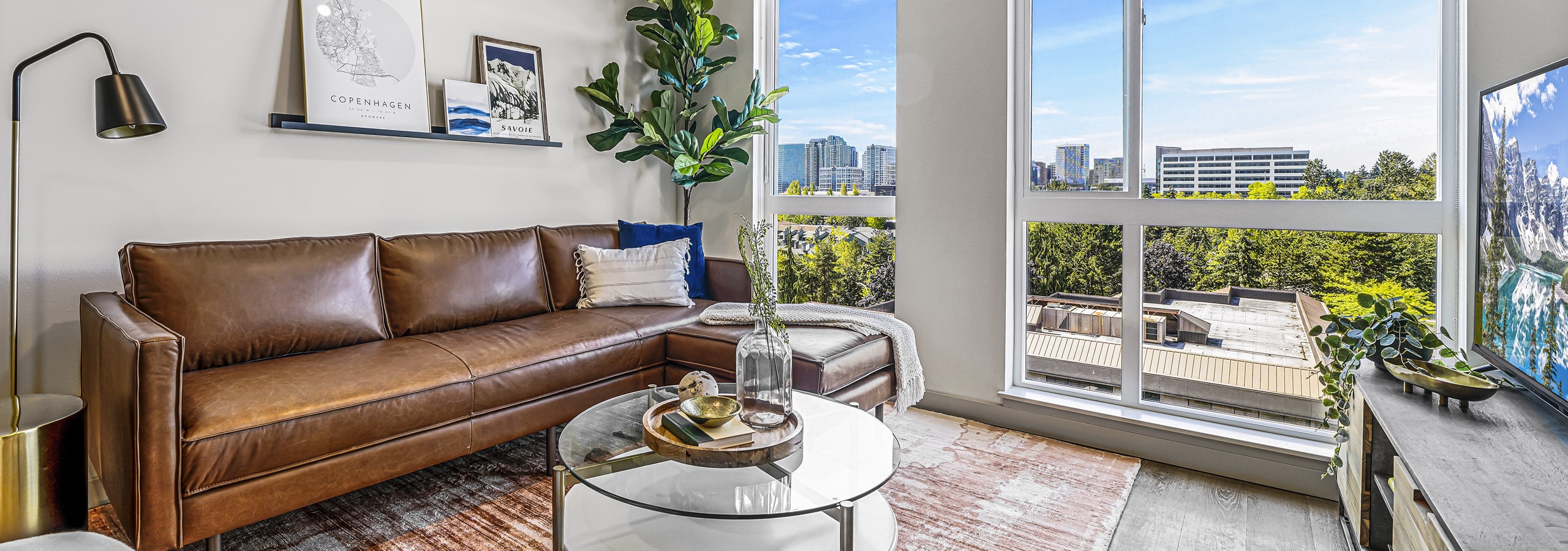 Living room with leather couch and floor to ceiling windows and dark wood style flooring at AMLI Spring District apartments