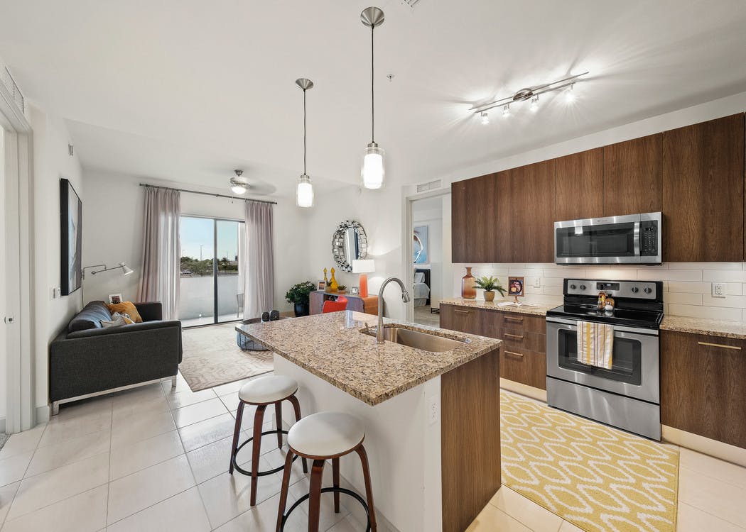 Interior view of AMLI 8800 apartment island kitchen with stainless steel appliances, granite counters and dark wood cabinetry