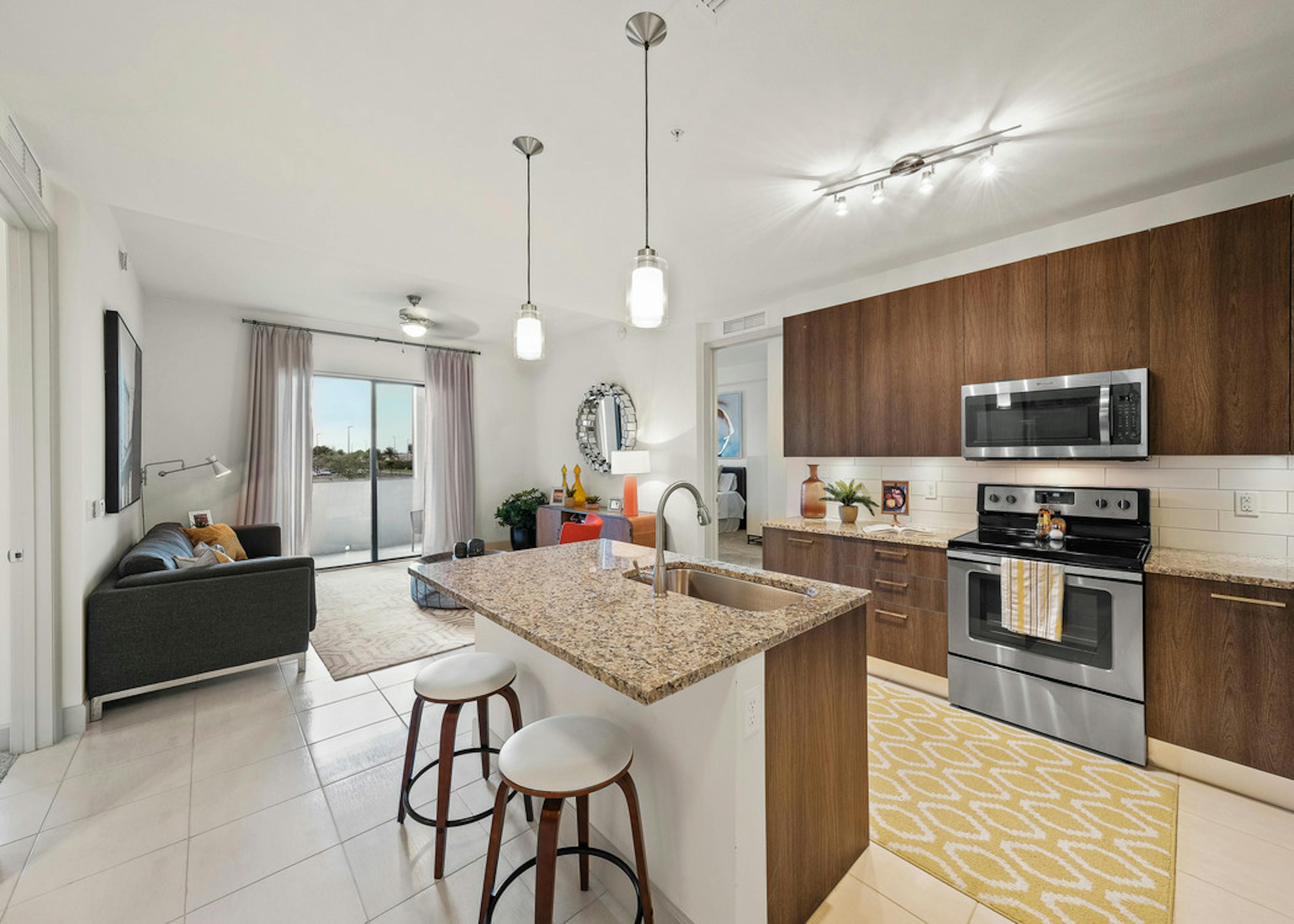 Interior view of AMLI 8800 apartment island kitchen with stainless steel appliances, granite counters and dark wood cabinetry