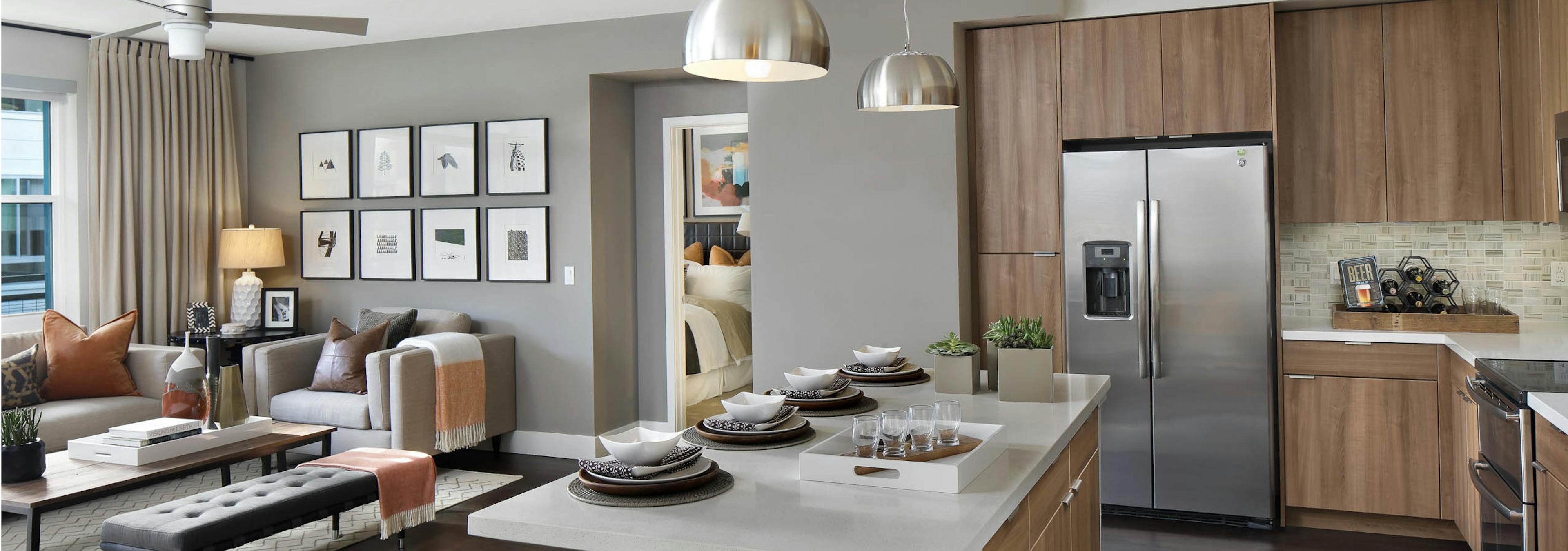 Interior of AMLI Uptown Orange apartment kitchen with quartz counters flowing into a furnished living room with ceiling fan