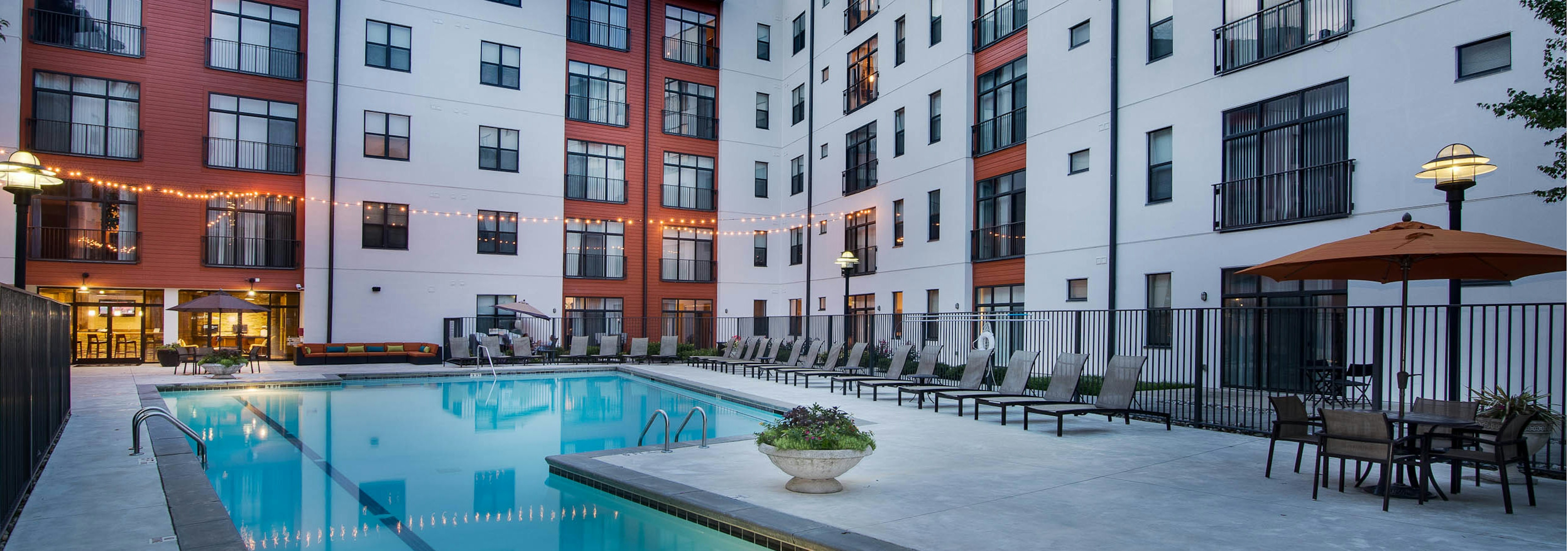 Dusk view of AMLI Old 4th Ward pool with lights reflecting from the fitness center surrounded by lounge chairs