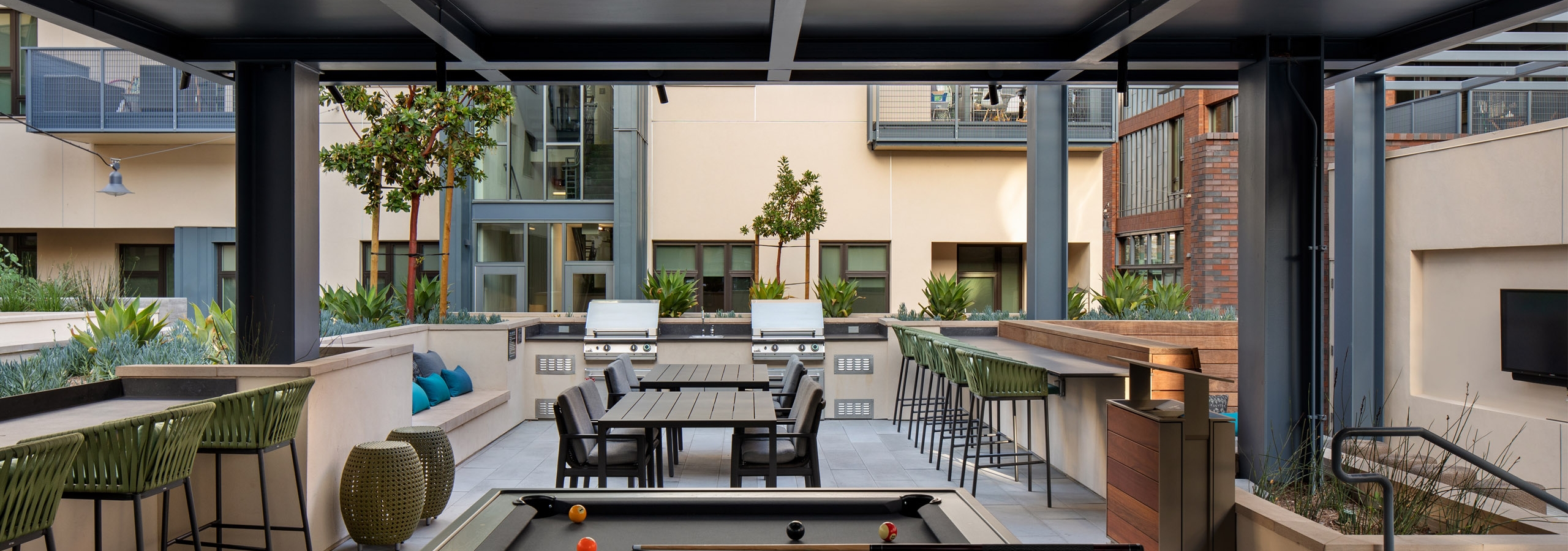 Pool courtyard at AMLI Old Pasadena apartments with two BBQ grills and various seating areas and billiard table