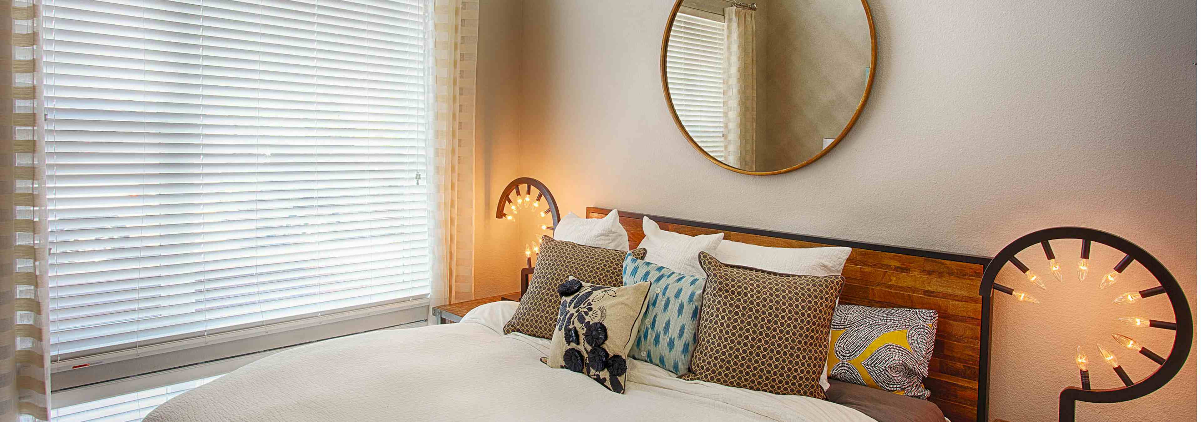 A bedroom at AMLI Denargo Market apartments featuring a bed with a wooden head board and a circular mirror and large window