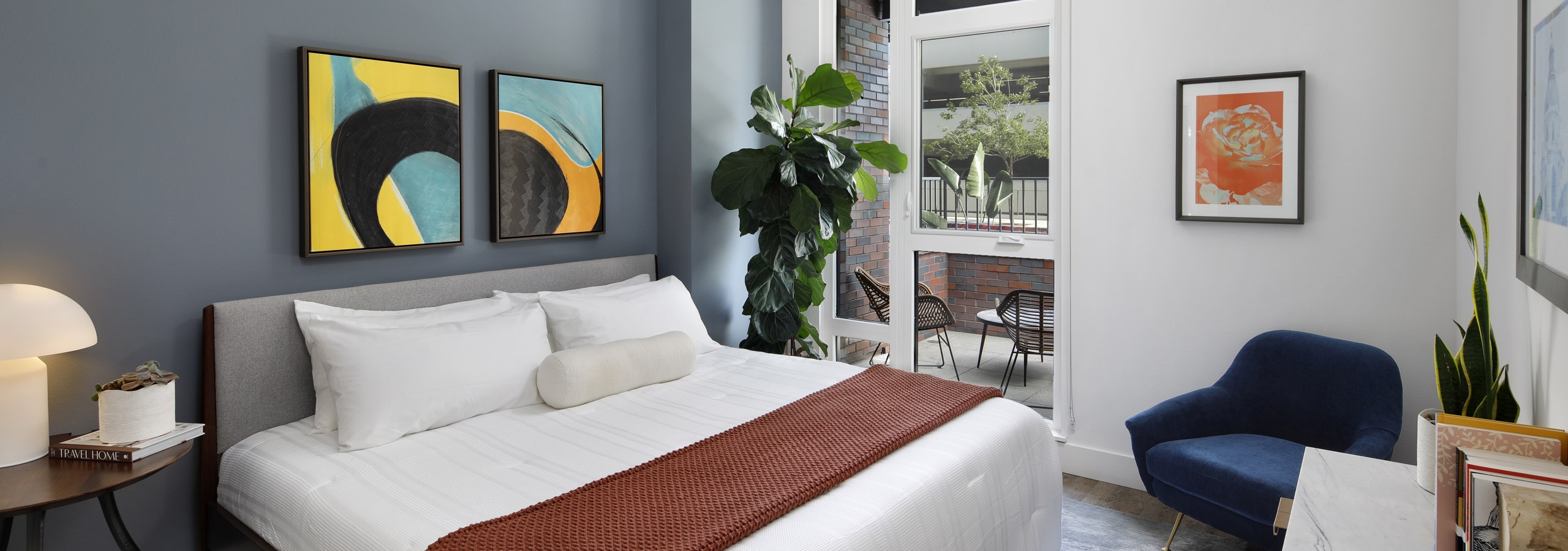 Spacious bedroom with light blue accent wall and large window overlooking the furnished patio at AMLI Old Pasadena apartments