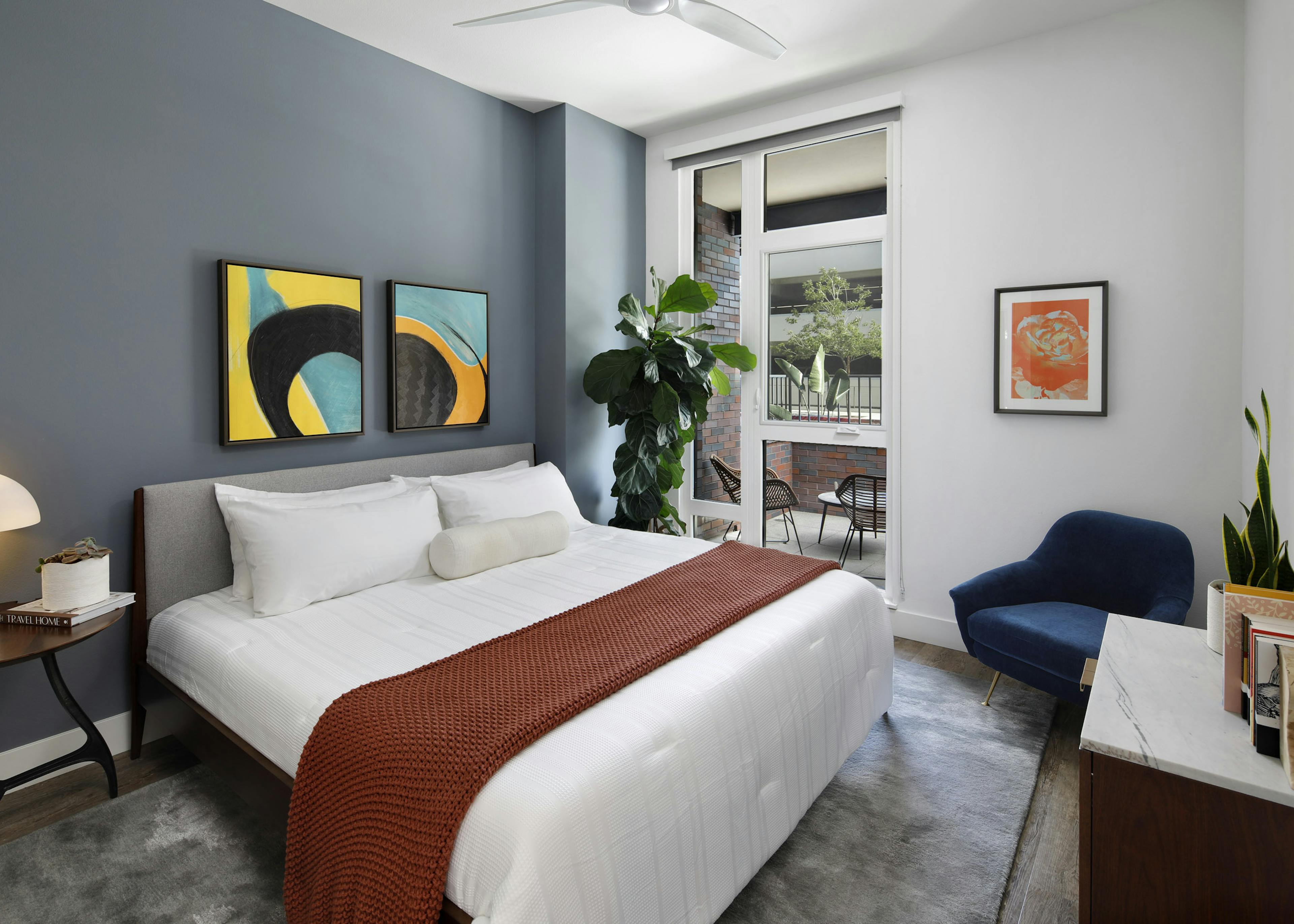 Spacious bedroom with light blue accent wall and large window overlooking the furnished patio at AMLI Old Pasadena apartments