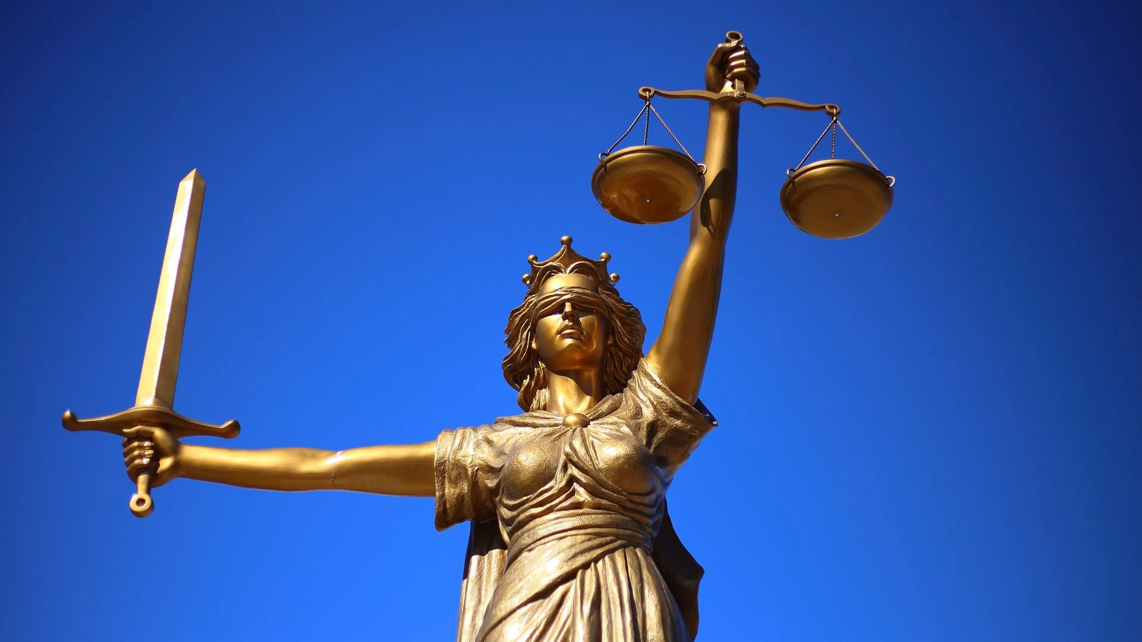A golden statue of a blindfolded woman with arms outstretched holding a sword and a set of scales