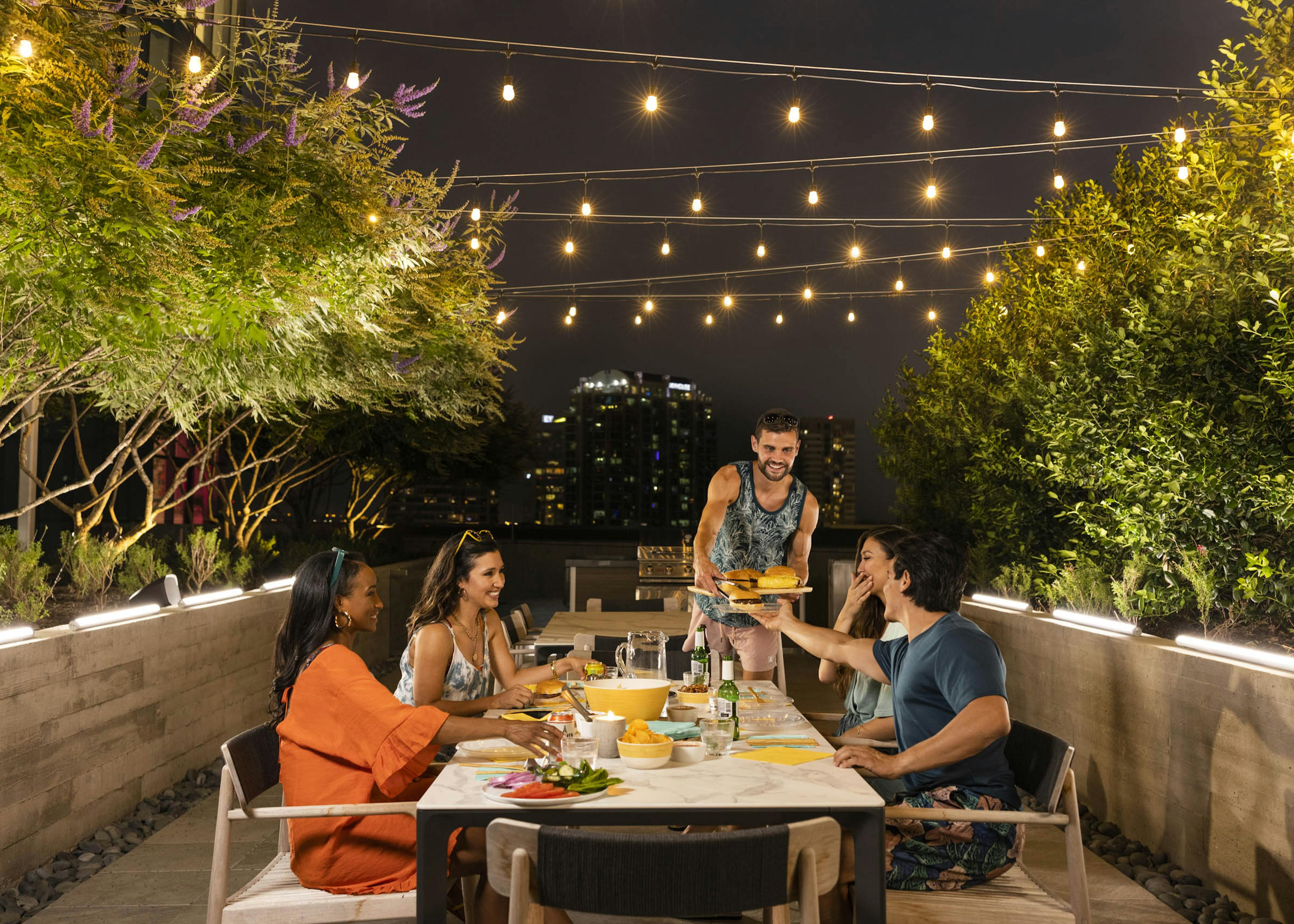 A group of friends eating at AMLI Fountain Place apartments outdoor resident entertainment area surrounded by greenery