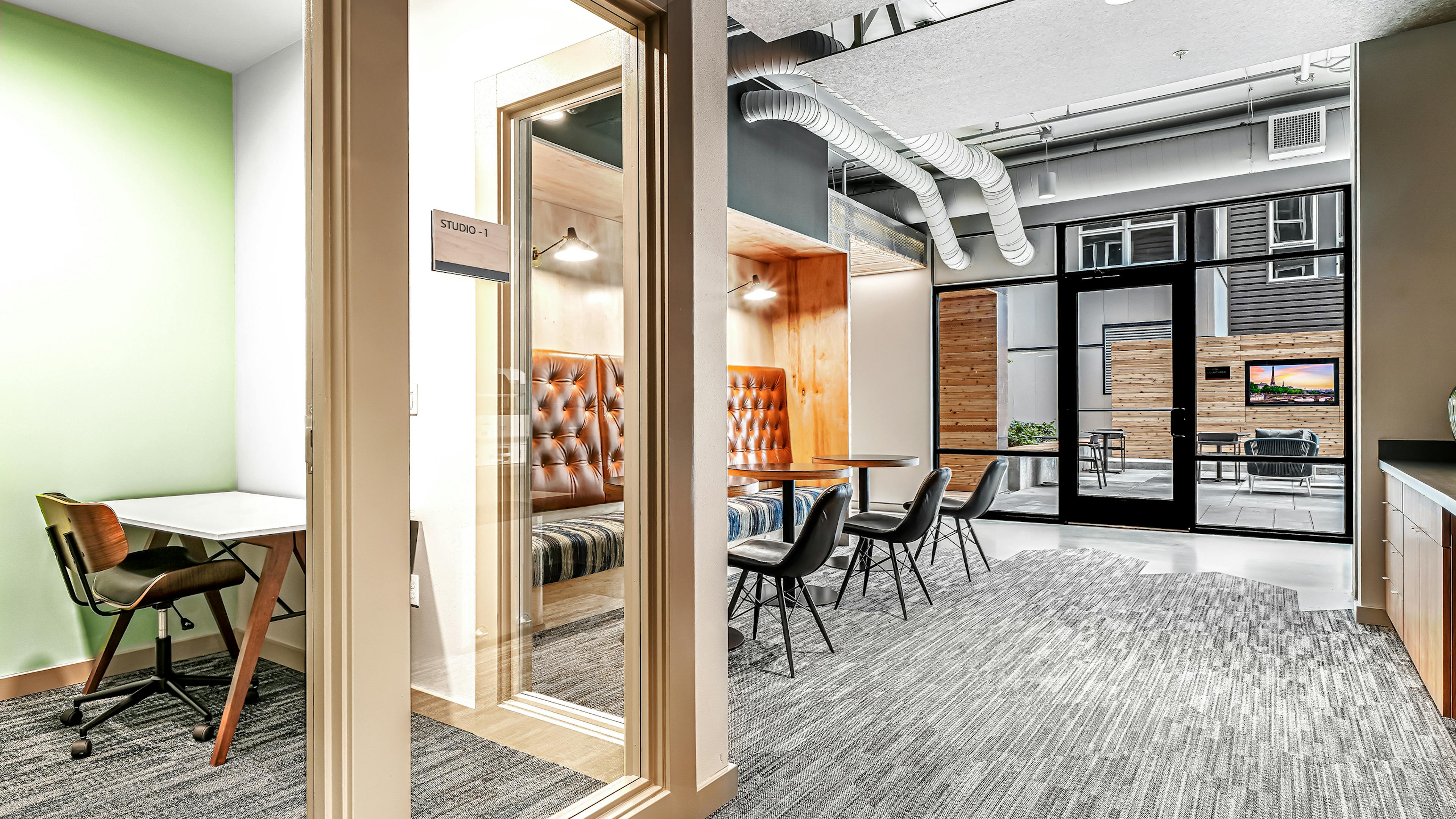 Interior view of AMLI Spring District coworking space with private office with glass door and booth and chairs with tables