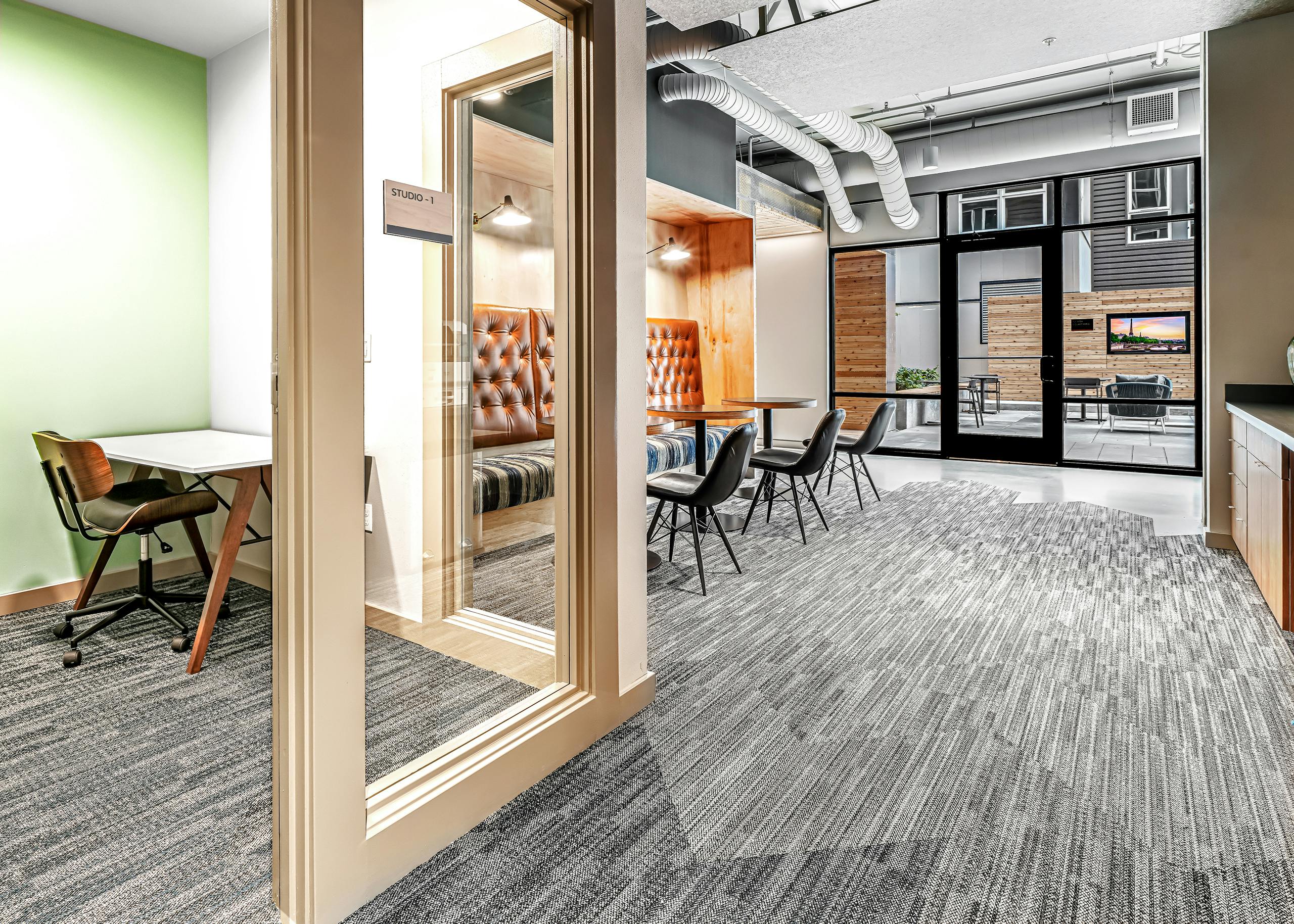 Interior view of AMLI Spring District coworking space with private office with glass door and booth and chairs with tables