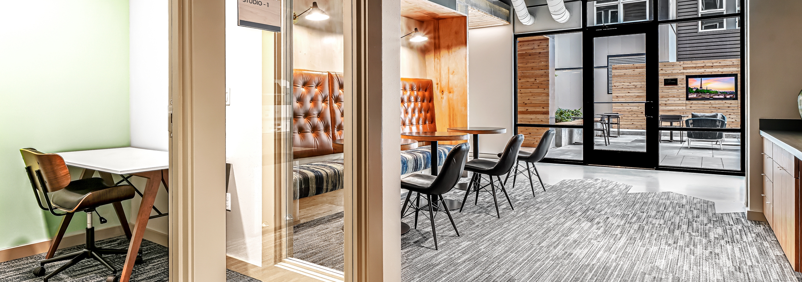 Interior view of AMLI Spring District coworking space with private office with glass door and booth and chairs with tables