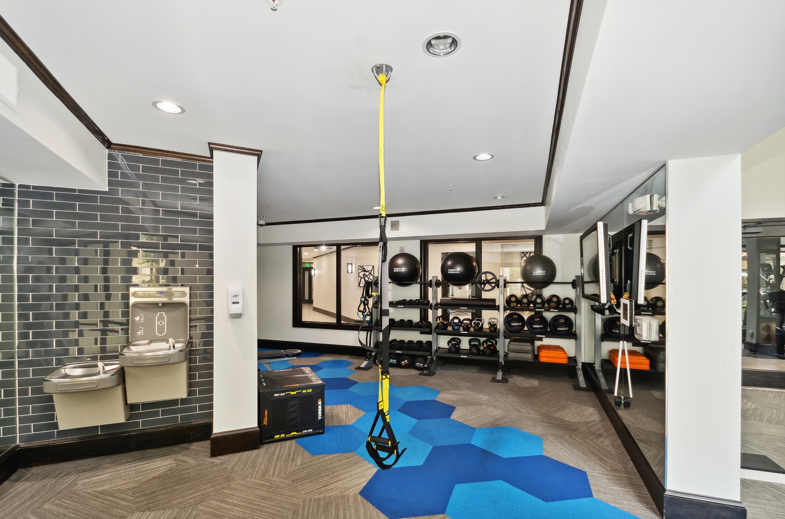 Fitness center at AMLI Campion Trail with weights on shelves and drinking fountains and and blue geometric pattern on floor