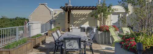 Rooftop at AMLI Evanston apartment community with outdoor dining set up in front of large potted plants with red flowers