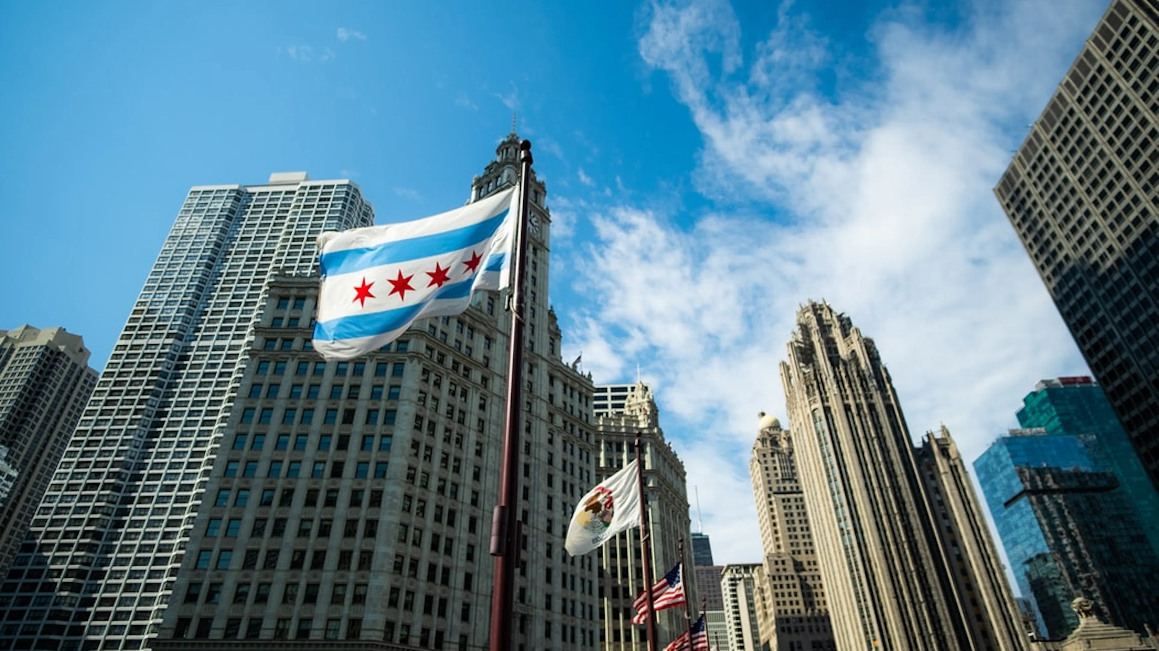 The Chicago flag flying in the wind on a flagpole with Downtown Chicago in the background