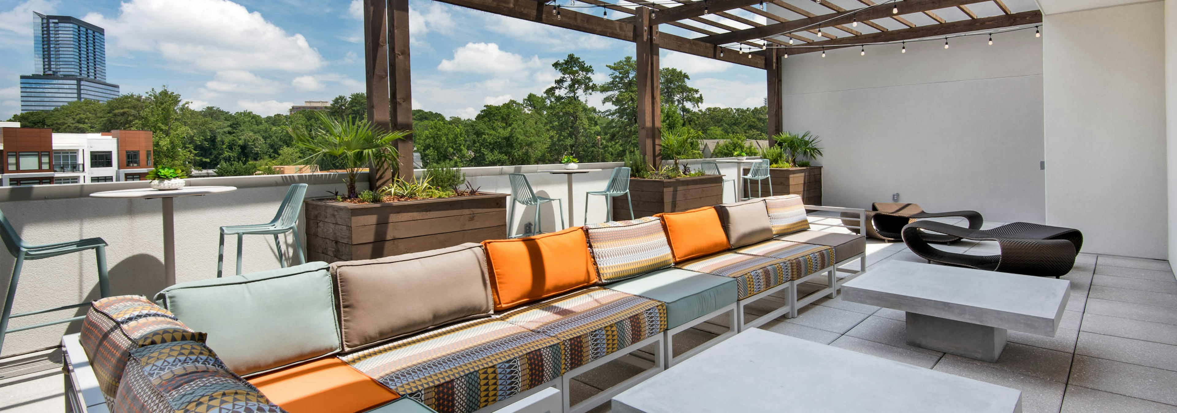 Long outdoor sofa with orange, tan and mint cushions under a pergola on the AMLI Buckhead skydeck with a bright daytime view