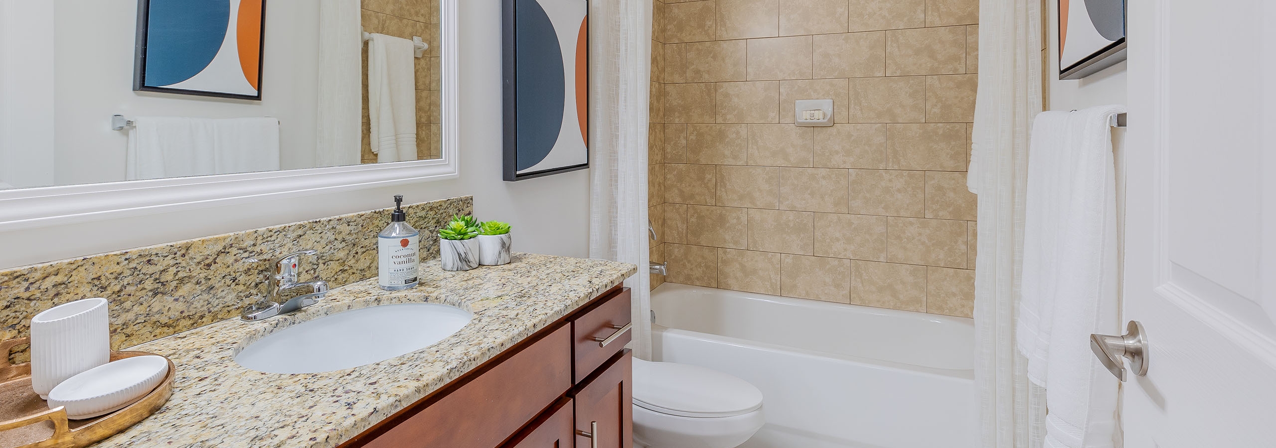 Interior view of AMLI Toscana Place apartment bathroom with wood vanity with large mirror and granite counter and soaking tub