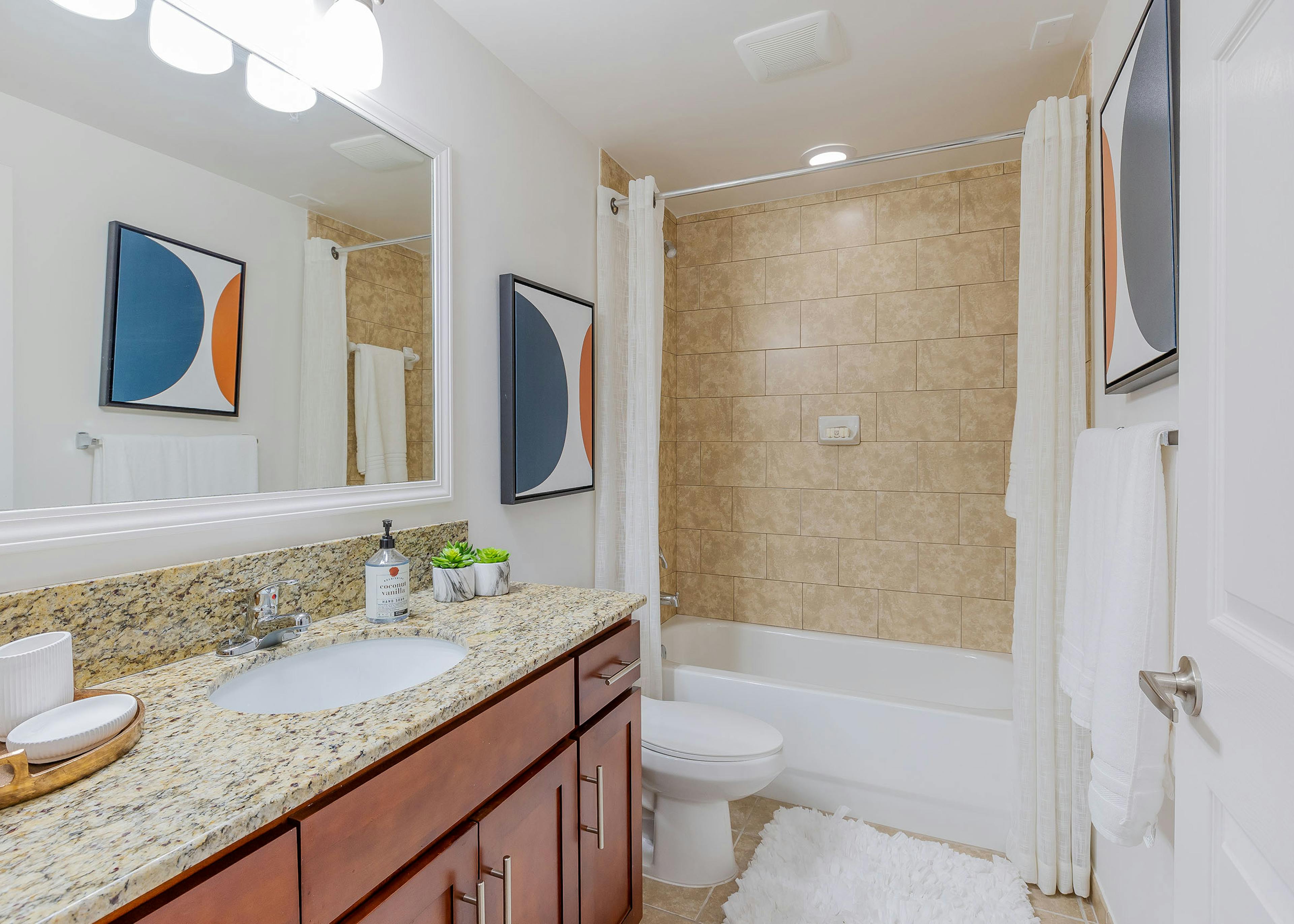 Interior view of AMLI Toscana Place apartment bathroom with wood vanity with large mirror and granite counter and soaking tub