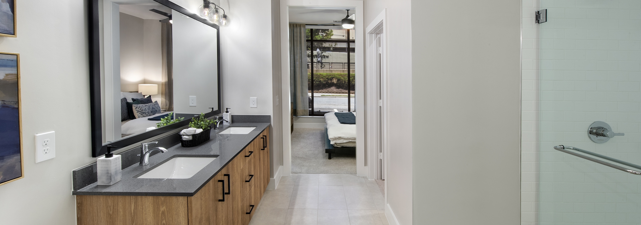 Bathroom at AMLI Flatiron with black stone countertop on wood grain double vanity and large mirror above and view to bedroom