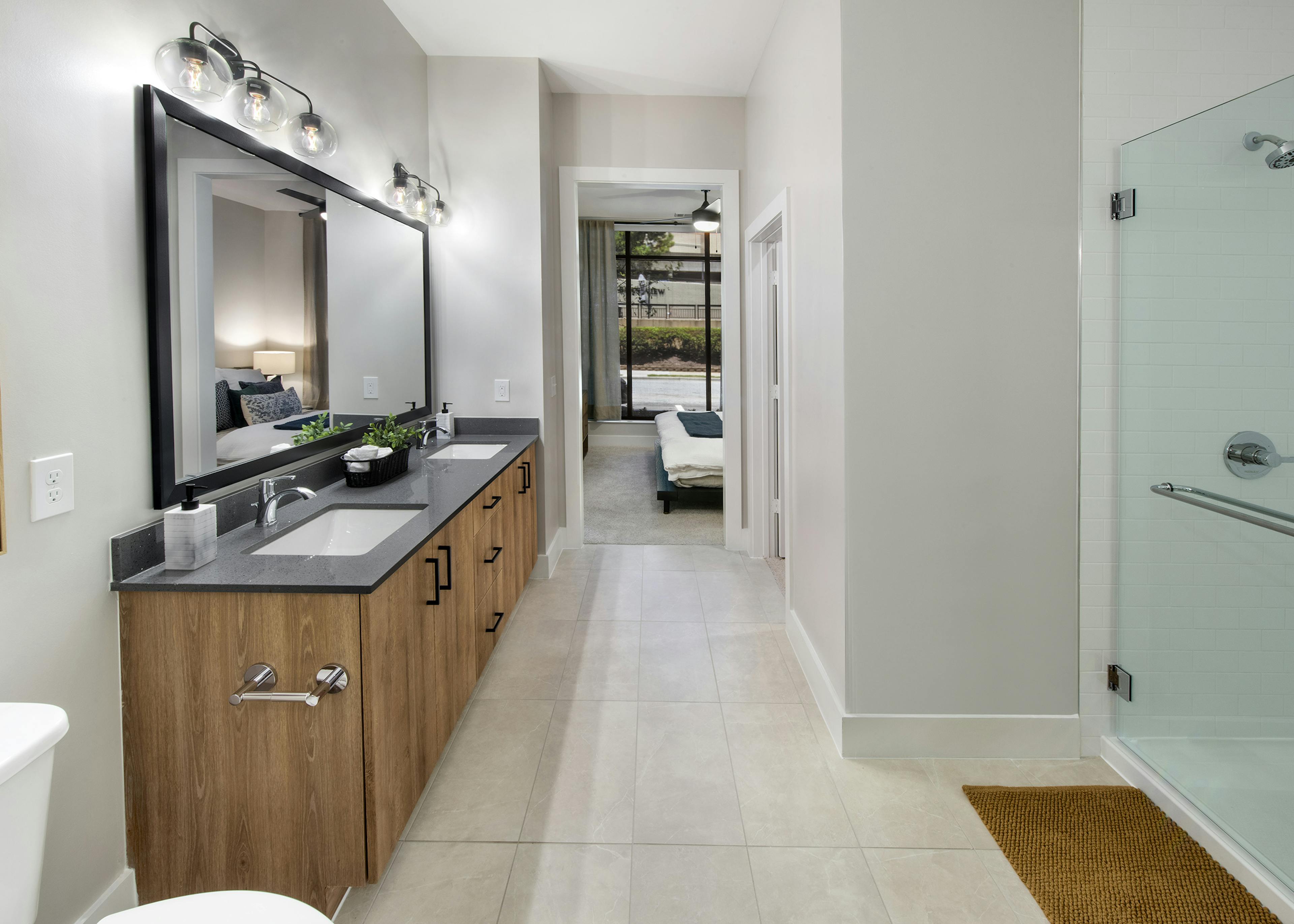 Bathroom at AMLI Flatiron with black stone countertop on wood grain double vanity and large mirror above and view to bedroom