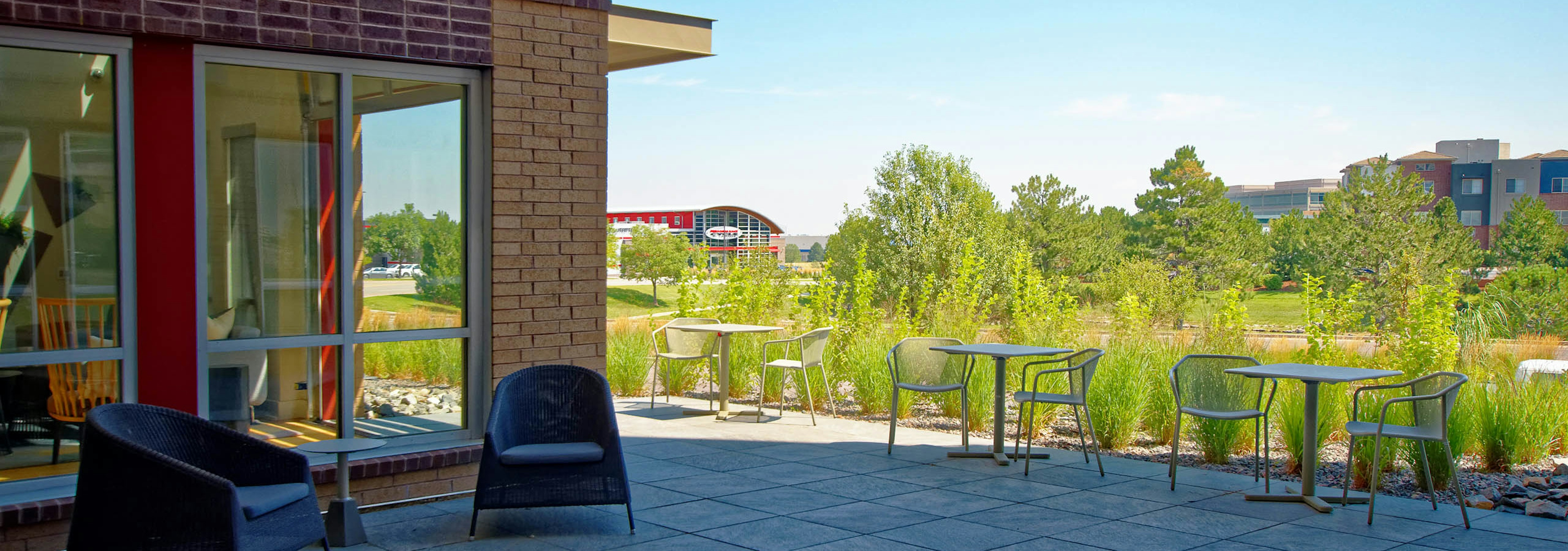 An outdoor lounge area at AMLI Dry Creek apartments with tables and chairs with view of several lush green trees and blue sky