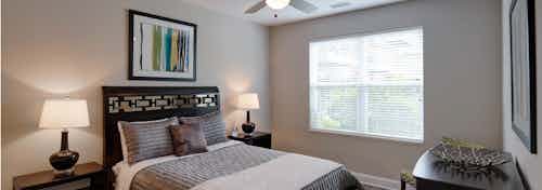 Interior of AMLI Deerfield apartment bedroom with ceiling fan and window furnished with bed and two nightstands and dresser