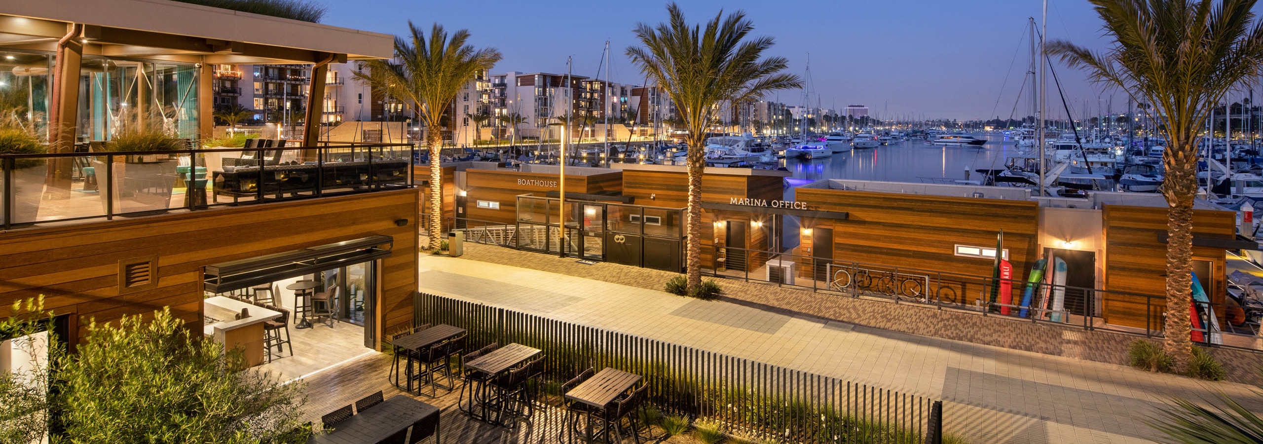 Panoramic evening view of the marina and boats and palm trees and peek into the lit up Jewel building at AMLI Marina Del Rey