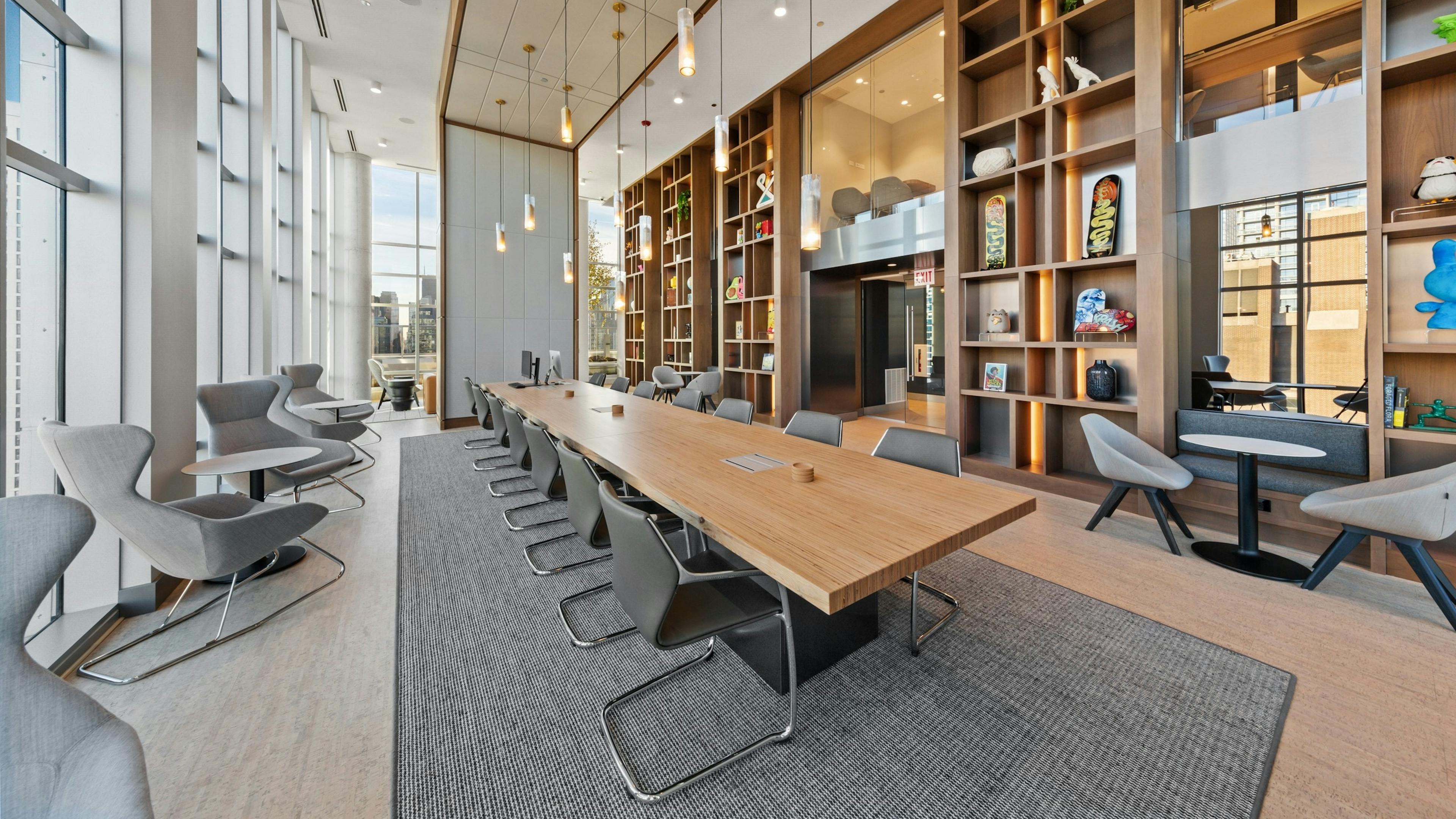 Luxurious collab space amenity at AMLI 808 featuring floor to ceiling windows and a modern table in front of sleek shelving